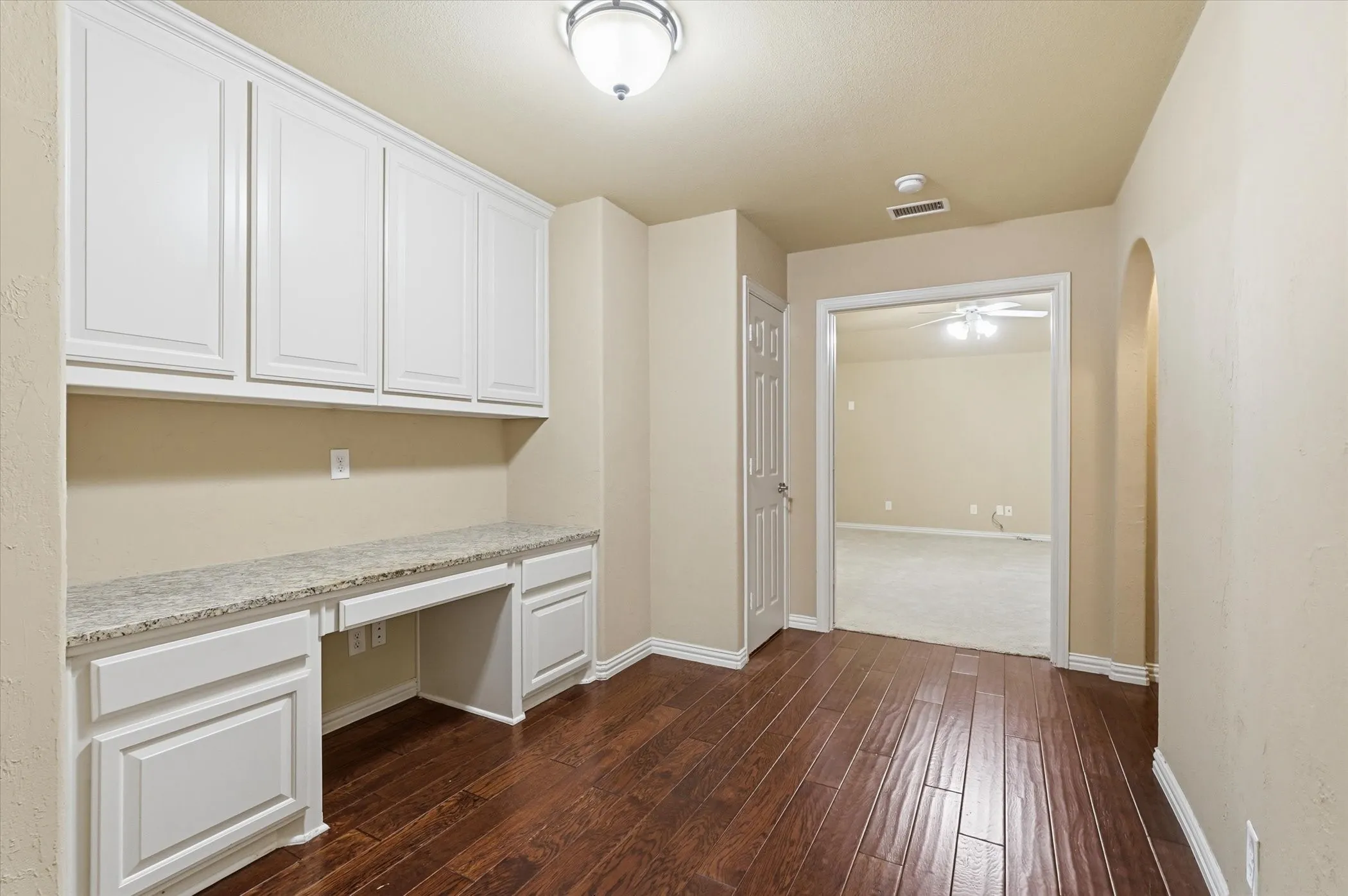 Unfurnished office featuring built in study area, dark wood-style flooring, a ceiling fan, and arched walkways