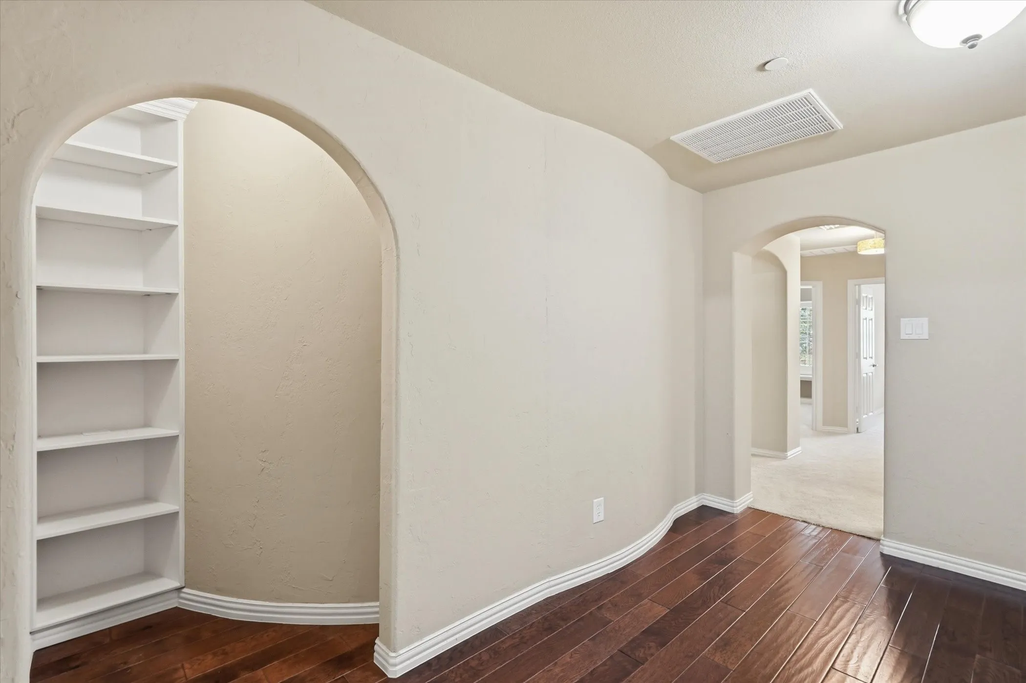 Spare room with arched walkways and dark wood-type flooring