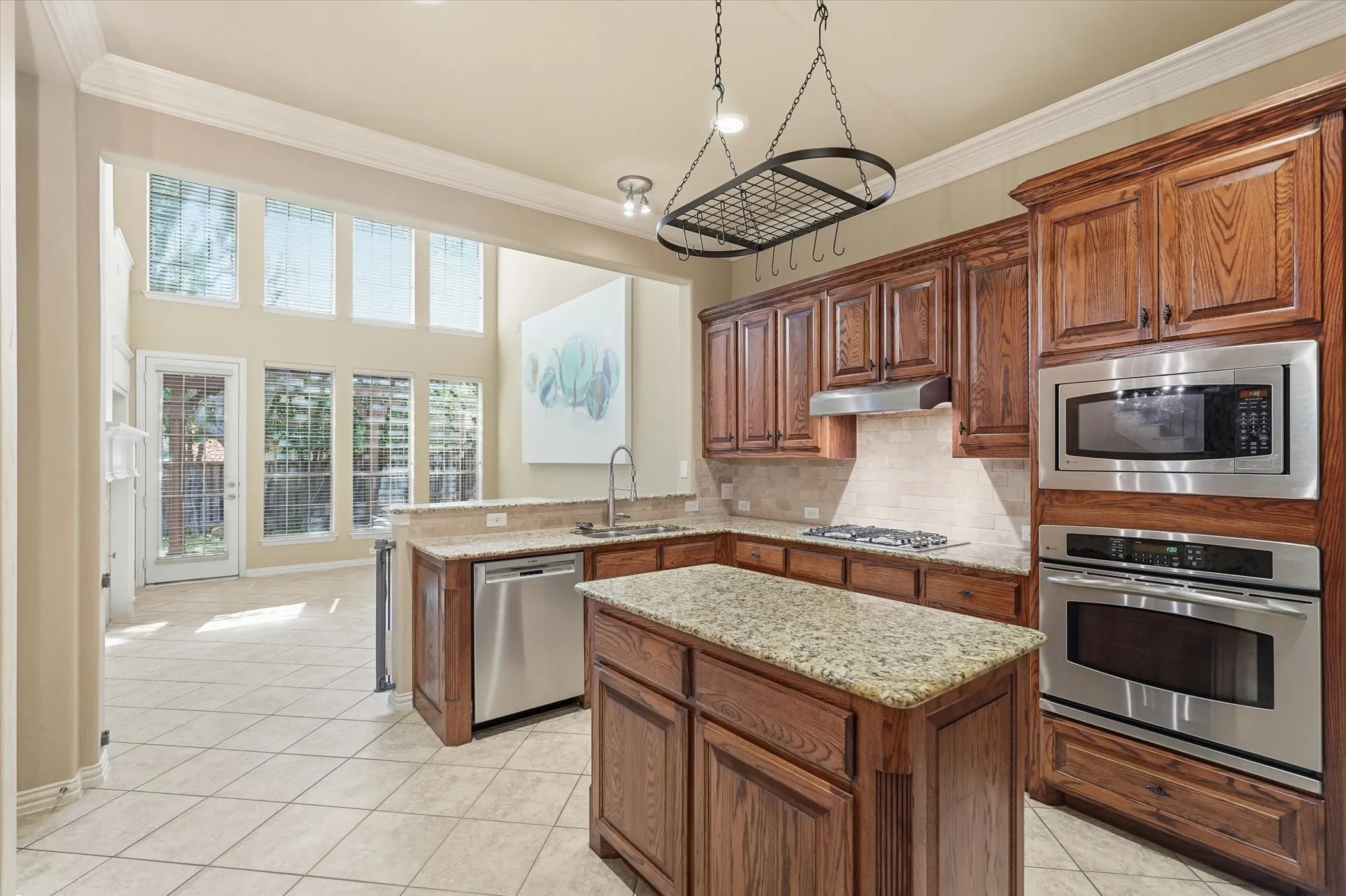 Kitchen with stainless steel appliances, a peninsula, crown molding, light stone counters, and light tile patterned floors