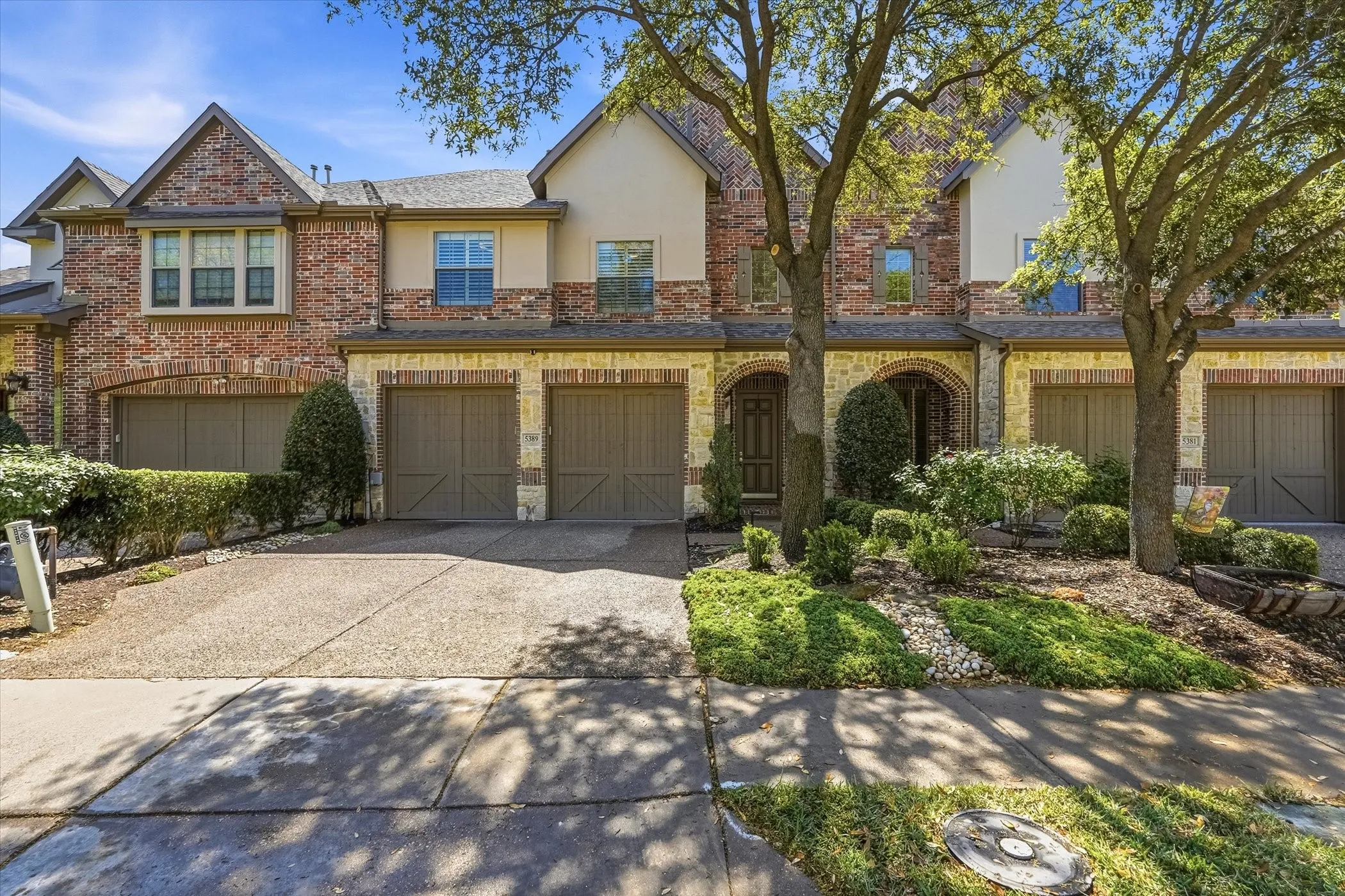 View of front facade featuring brick siding, driveway, stucco siding, an attached garage, and stone siding