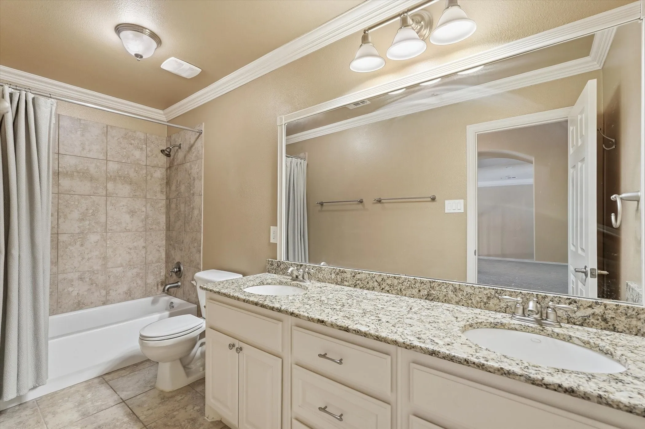 Bathroom featuring double vanity, shower / tub combo, ornamental molding, and light tile patterned floors