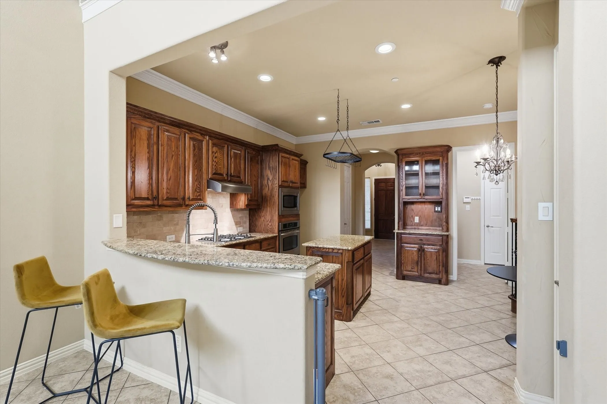 Kitchen featuring decorative backsplash, arched walkways, light tile patterned floors, a peninsula, and ornamental molding