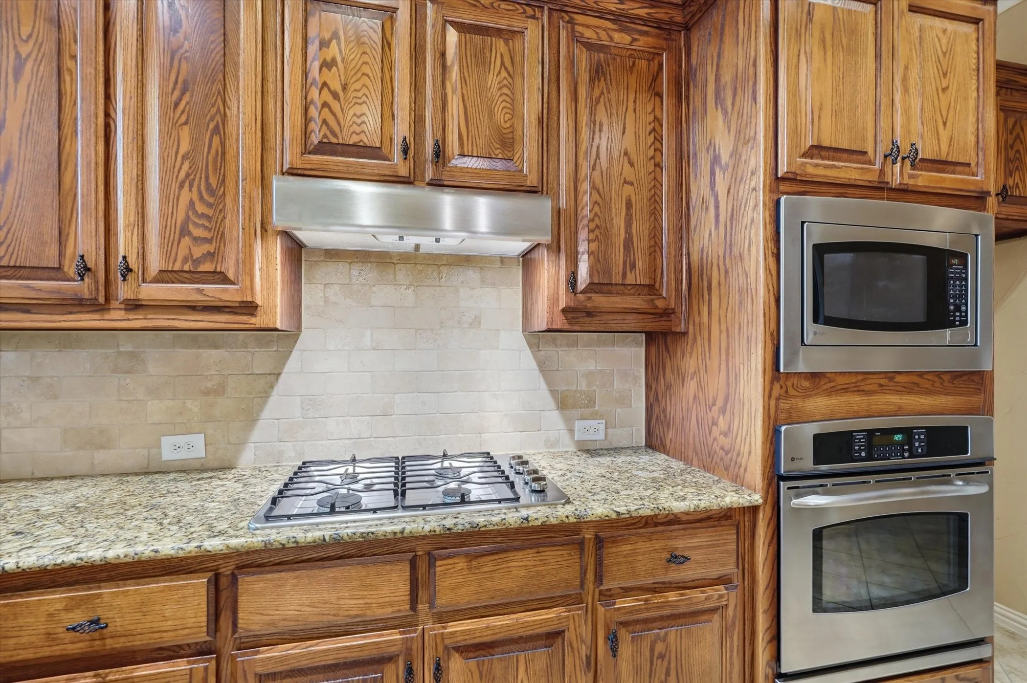 Kitchen featuring stainless steel appliances, light stone counters, wood finish cabinetry, and tasteful backsplash