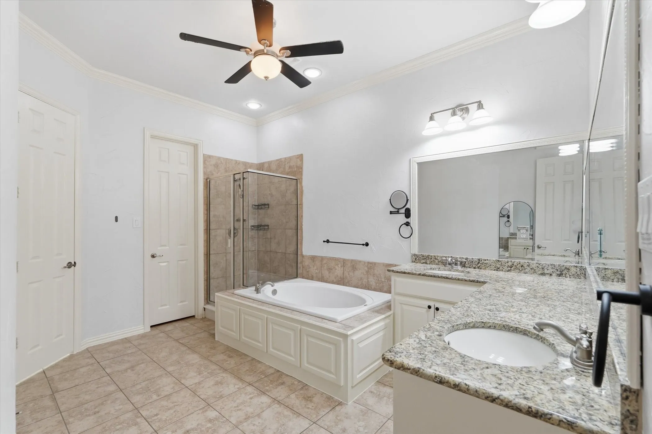 Full bathroom featuring double vanity, a stall shower, a garden tub, ornamental molding, and a ceiling fan