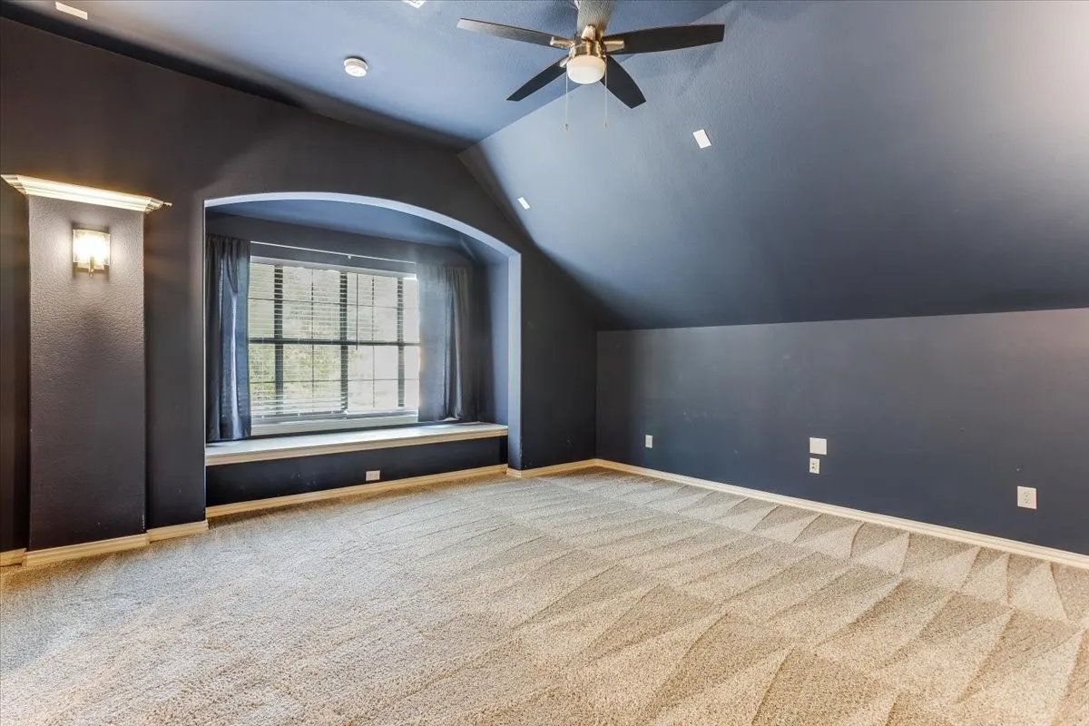 Arched window alcove with built-in bench, textured carpeting, sloped ceiling, and ceiling fan with integrated lighting
