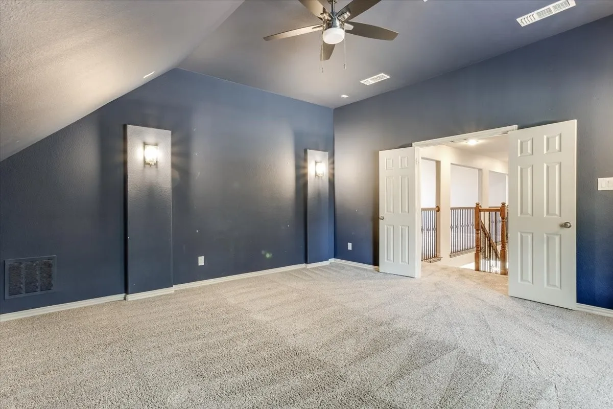 Carpeted flooring, sloped ceiling, ceiling fan with integrated lighting, wall sconces, and double doors