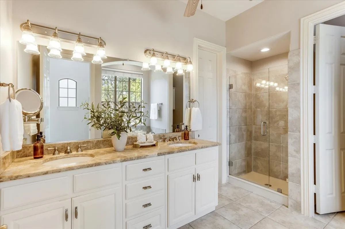 Dual vanity with undermount sinks and extensive countertop space, individual mirrors, and a glass-enclosed shower with tiled walls