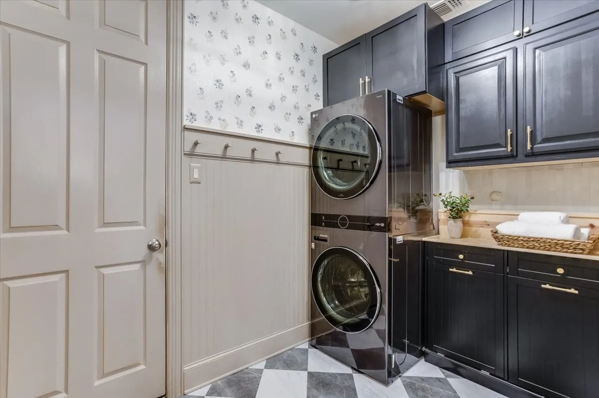 Laundry area featuring dark cabinetry with gold-tone hardware, a light wood-finish countertop, and a checkerboard floor