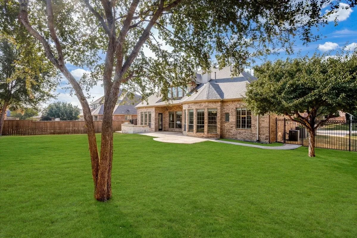 Expansive green lawn with mature trees, brick exterior, stone patio, and a privacy fence