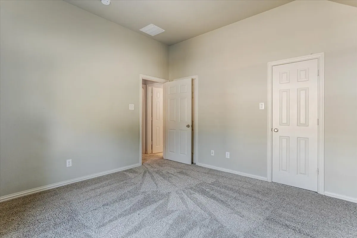 Vaulted ceiling, neutral wall tones, gray patterned carpeting, white trim, and a white paneled door