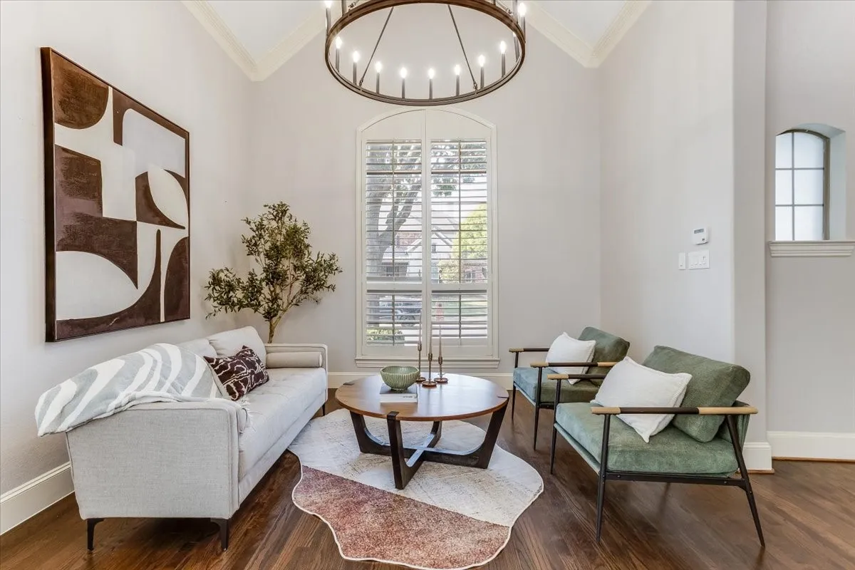 Double-height vaulted ceiling with crown molding, hardwood flooring, an arched window with plantation shutters, and a large circular chandelier