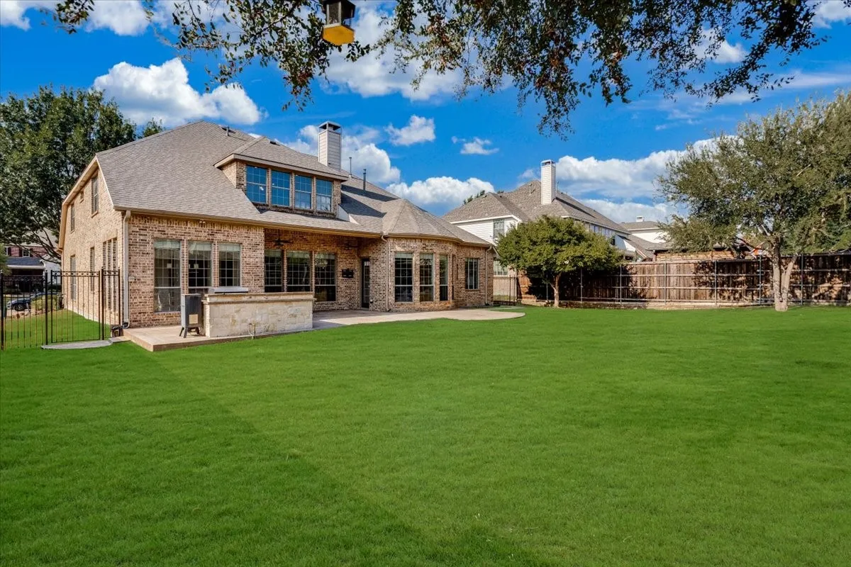 Expansive green lawn, brick exterior, multiple large windows, stone patio, and dormer window