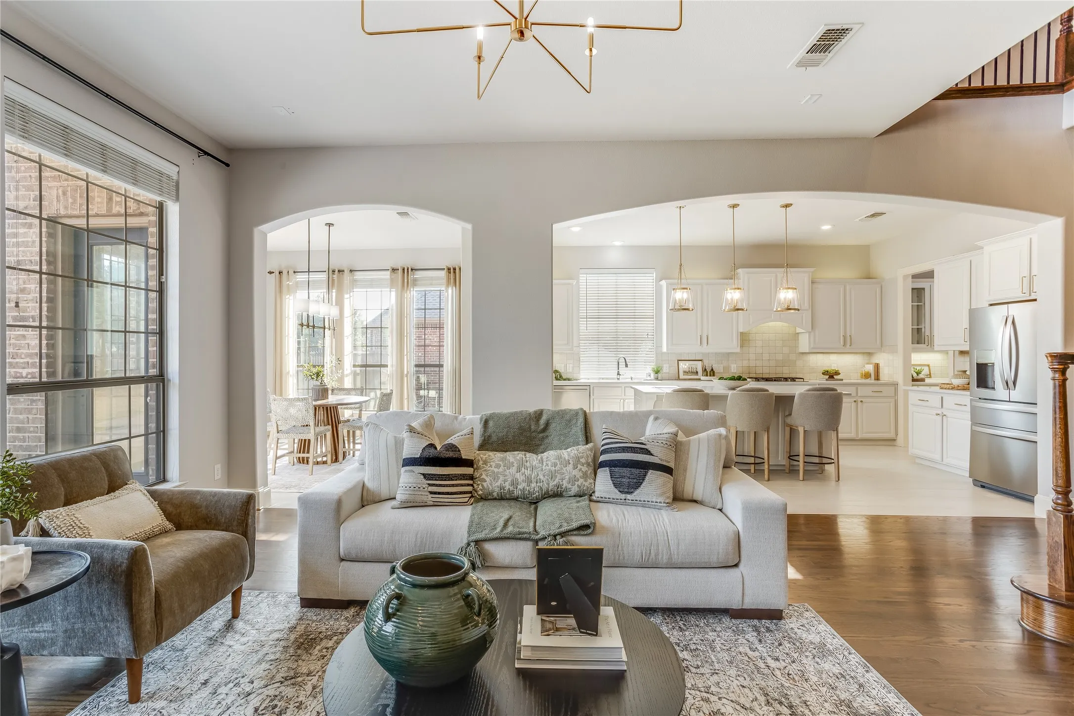 High ceilings with a decorative chandelier, expansive windows with black grids, arched doorways, wood-finish flooring, and a kitchen with white cabinetry and stainless steel appliances