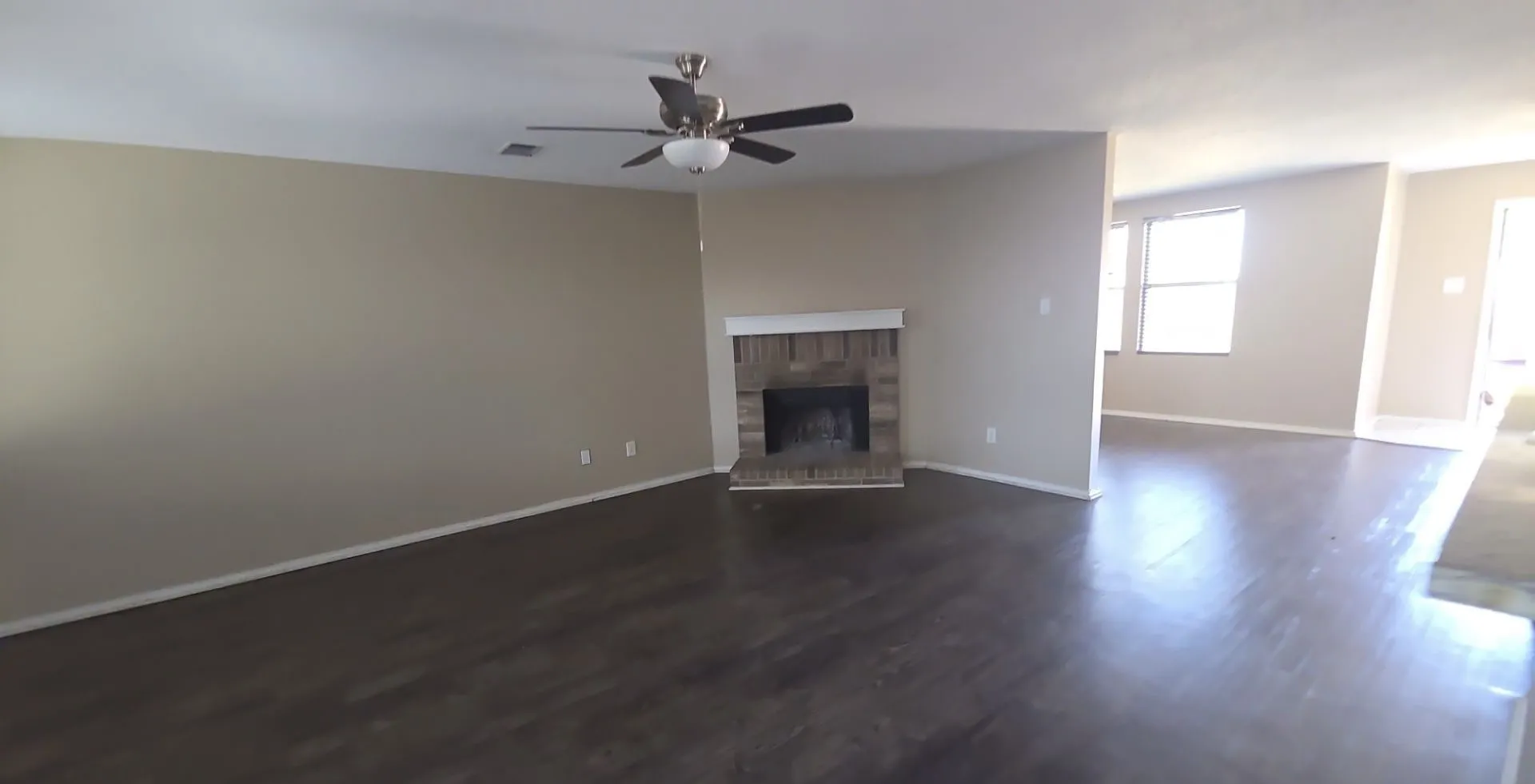 Wood-finish flooring, ceiling fan with integrated lighting, brick fireplace with mantel, and neutral wall tones