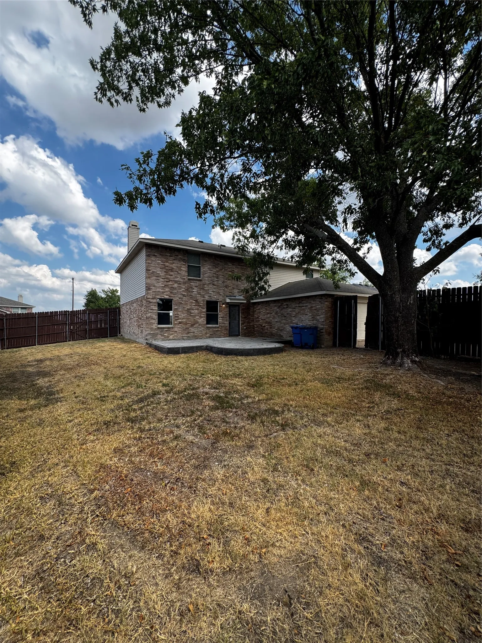 Expansive backyard featuring a mature tree, brick exterior, concrete patio, and privacy fencing