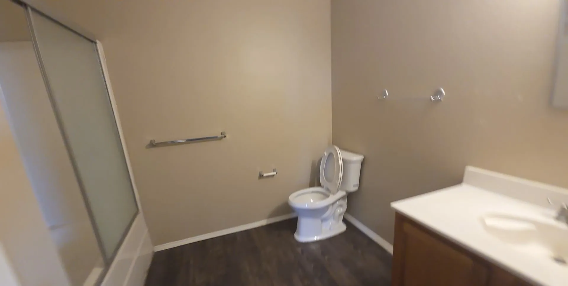 Bathroom featuring a shower with a sliding glass door, a toilet, a vanity with a white countertop, and wood-finish flooring
