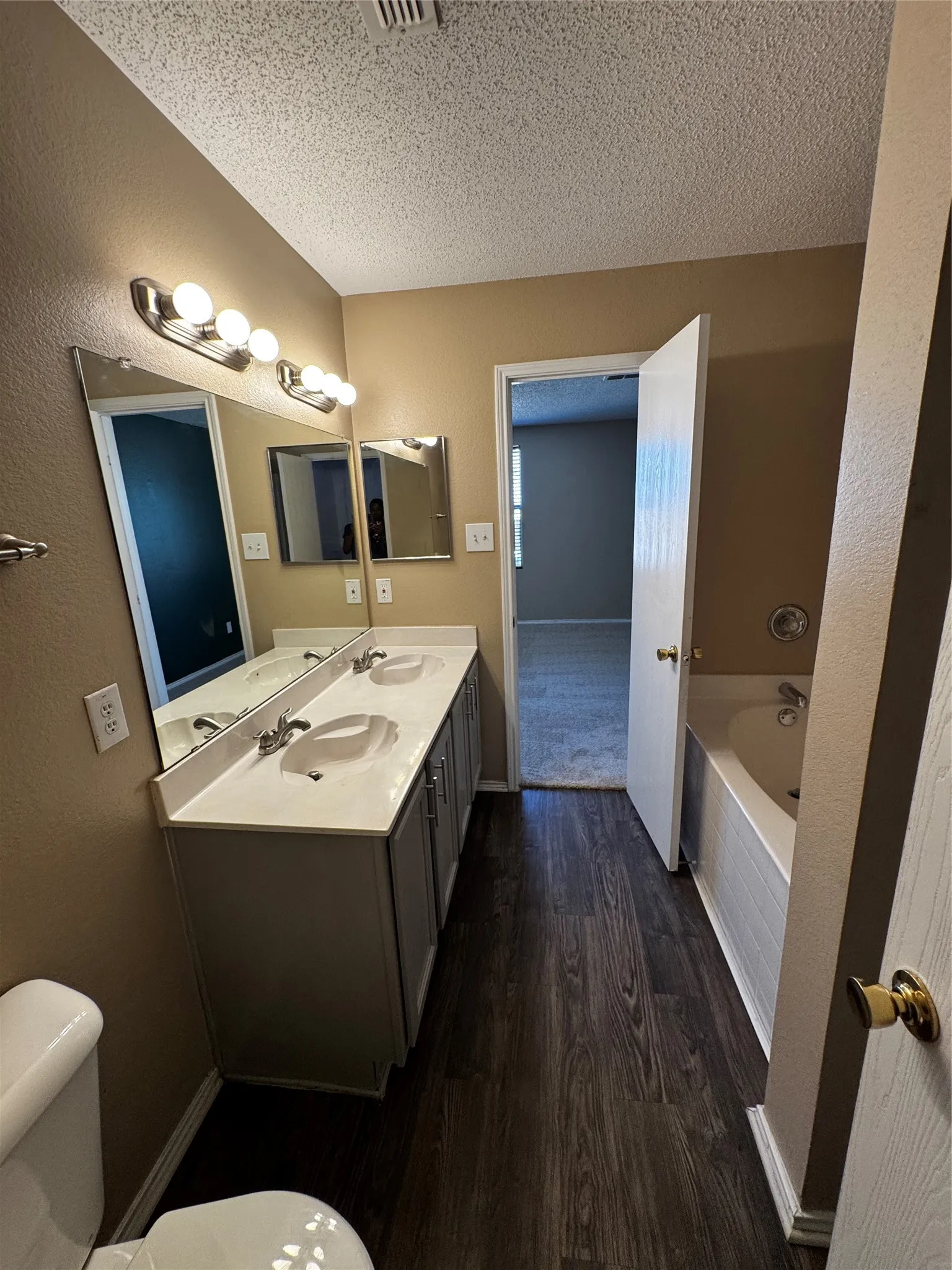Dual basin vanity with integrated sinks, wood-finish flooring, full-length vanity mirror, and built-in bathtub