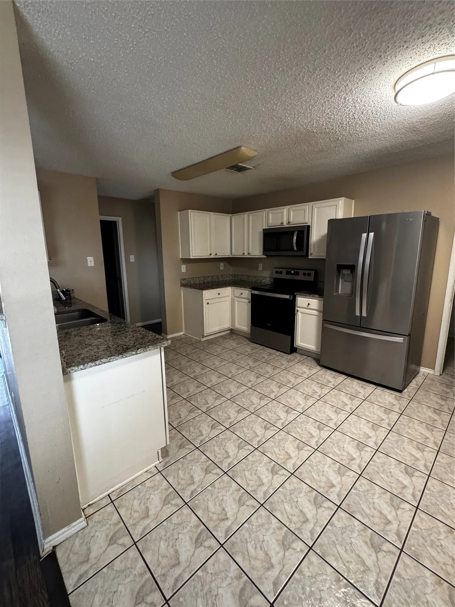 Kitchen featuring white cabinetry, stainless steel appliances, granite countertops, and tiled flooring