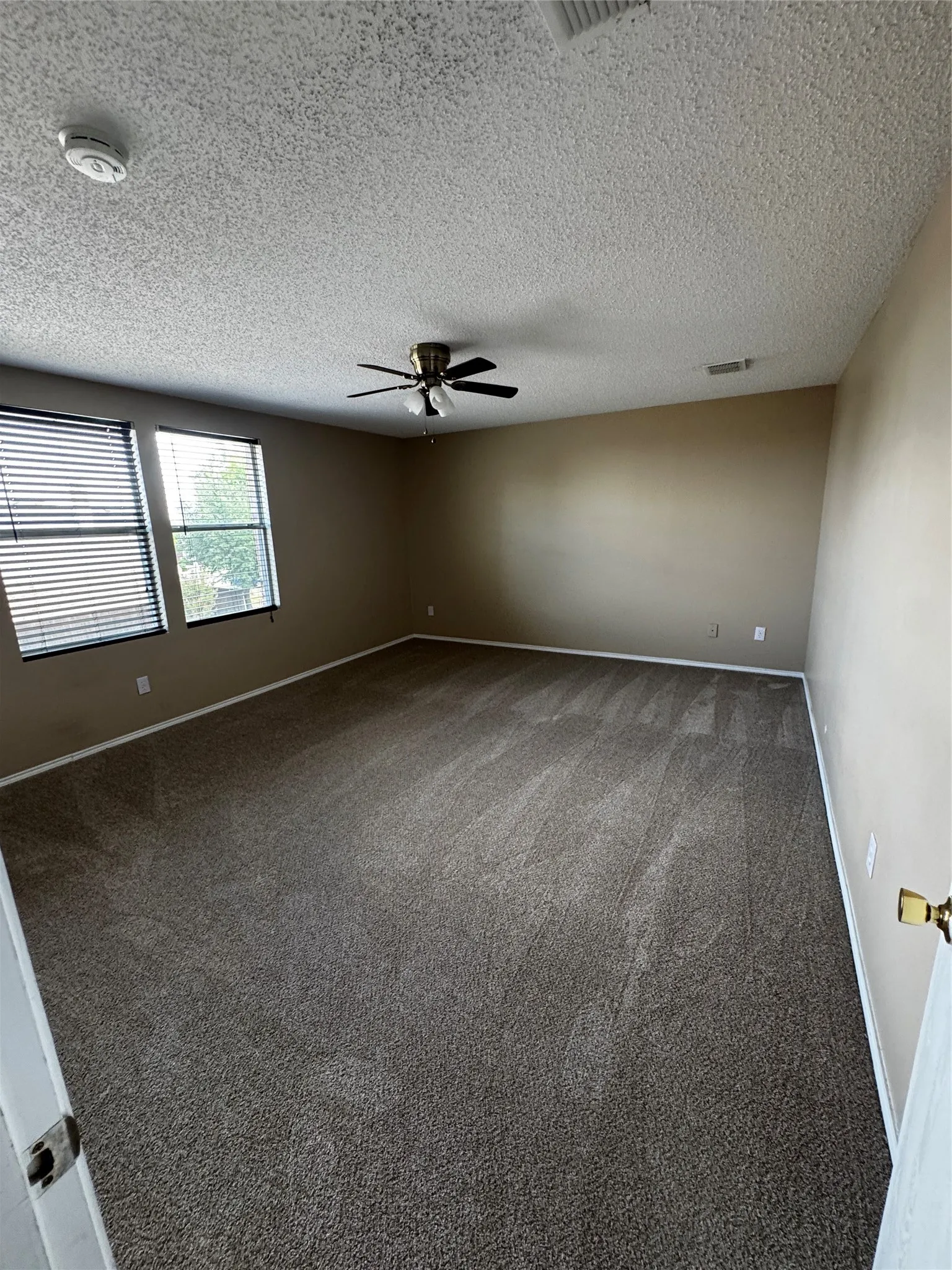 Plush carpeting, neutral wall tones, two windows with blinds, and a ceiling fan with integrated lighting