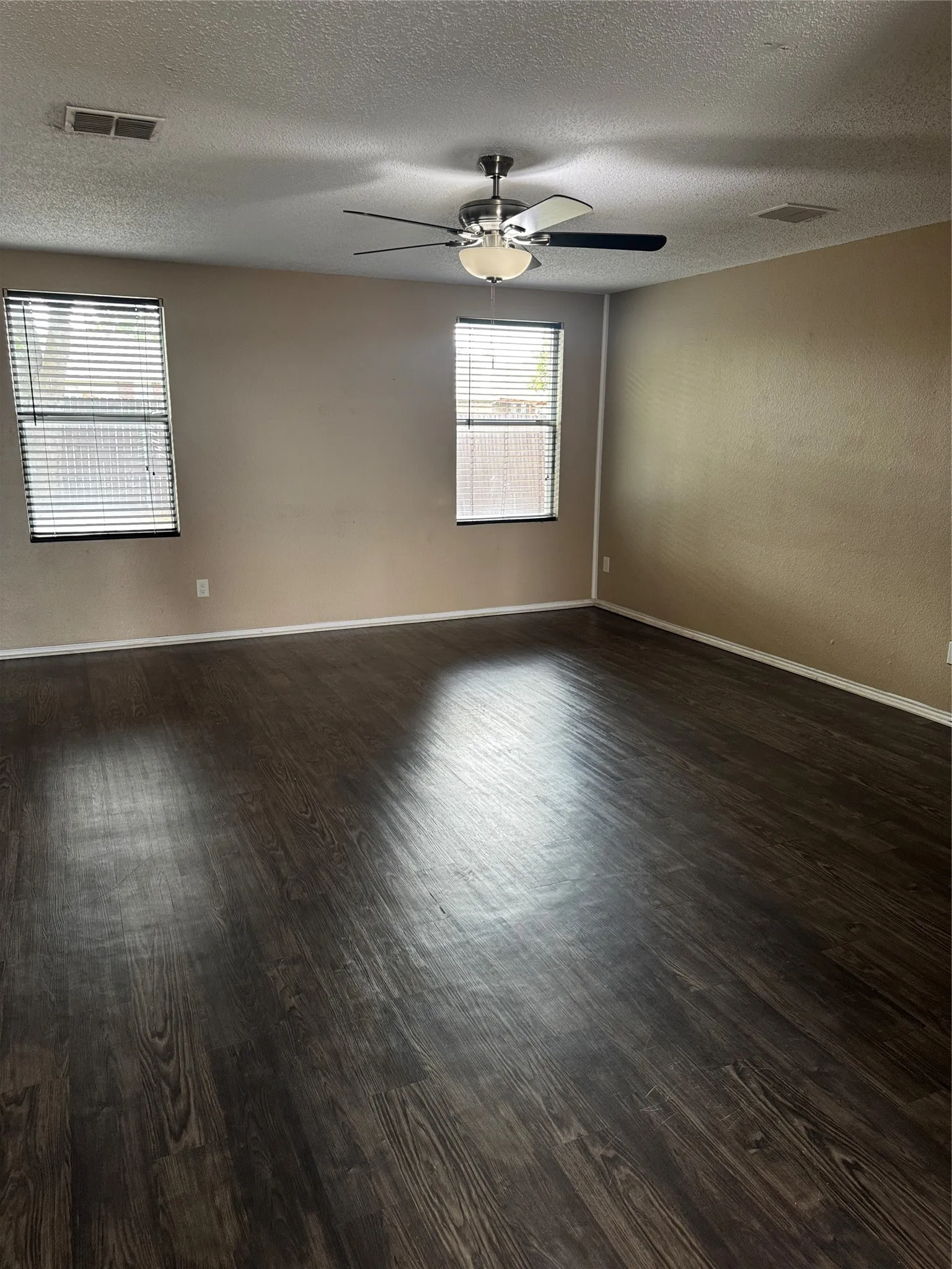 Wood-finish flooring, two windows with blinds, and a ceiling fan with integrated lighting