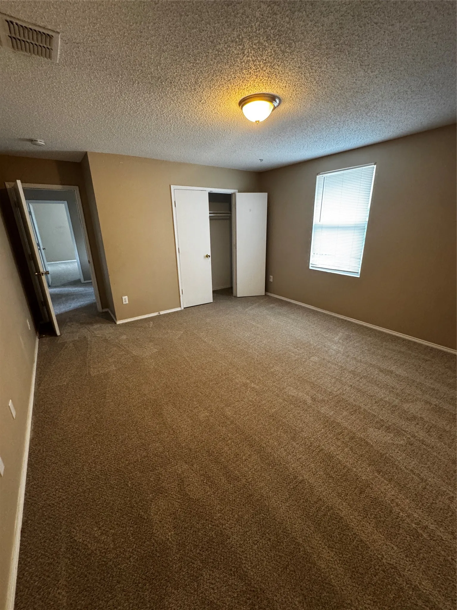 Spacious room featuring neutral carpeting, a dual-door closet, a window with blinds, and an overhead flush mount light fixture