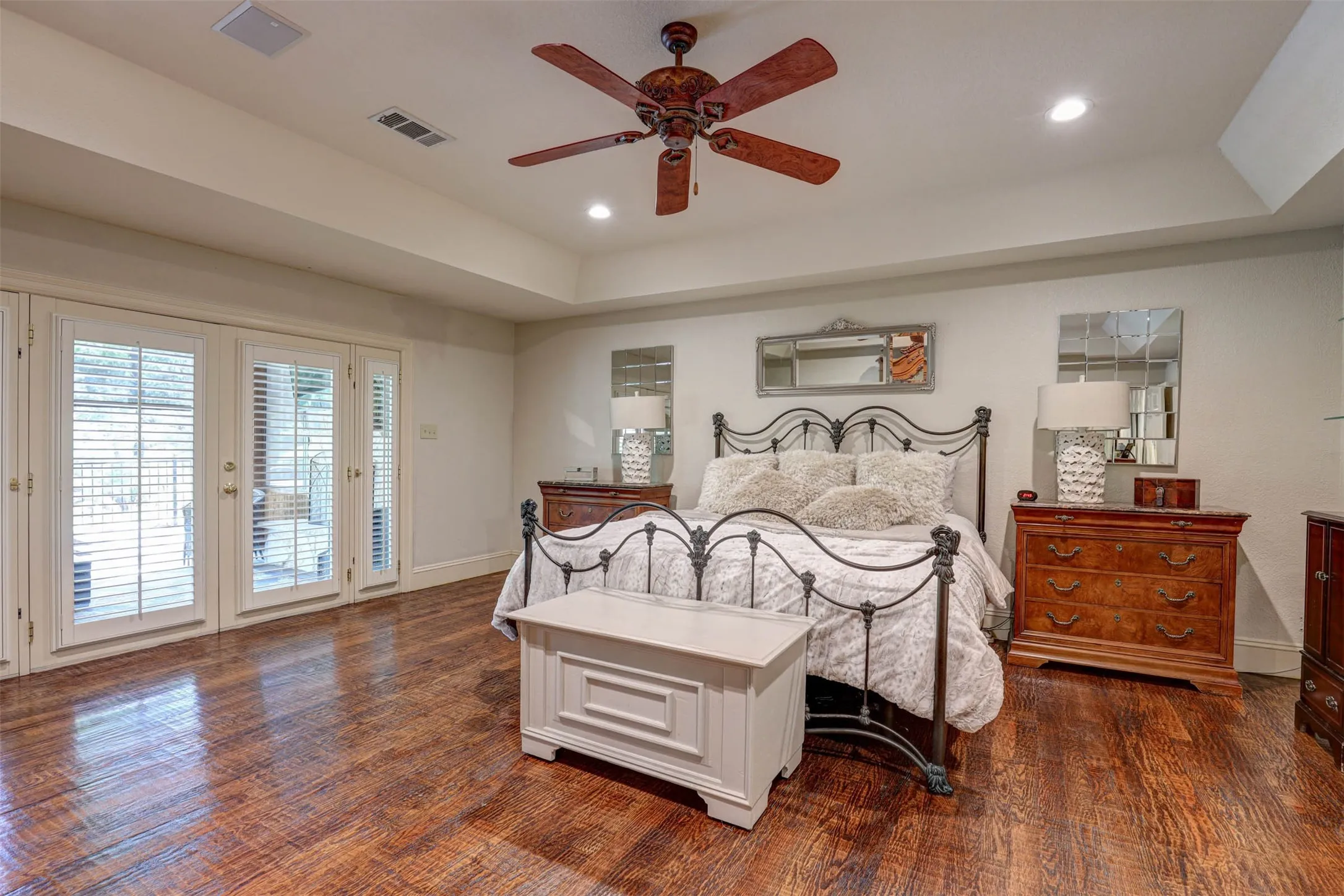 Spacious primary bedroom with raised tray ceiling, hardwood floors, and French doors to private owners retreat.