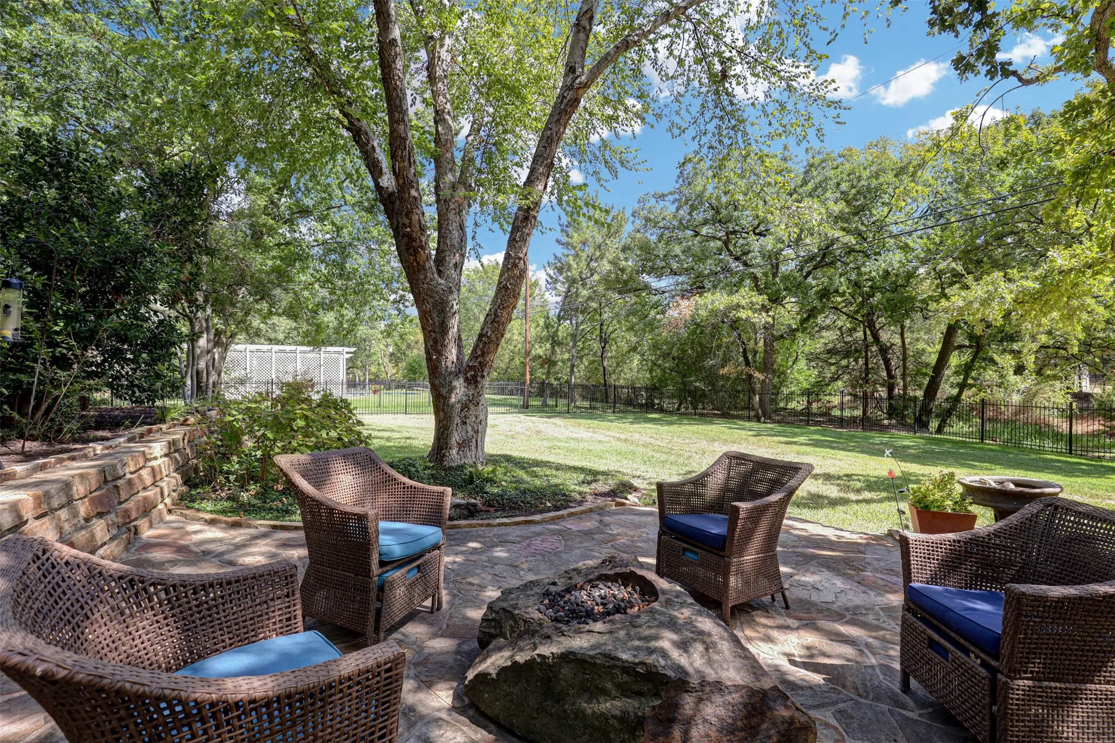 Stone patio with seating around a firepit, surrounded by mature trees and landscaped garden beds.Stone patio with seating around a firepit, surrounded by mature trees and landscaped garden beds.