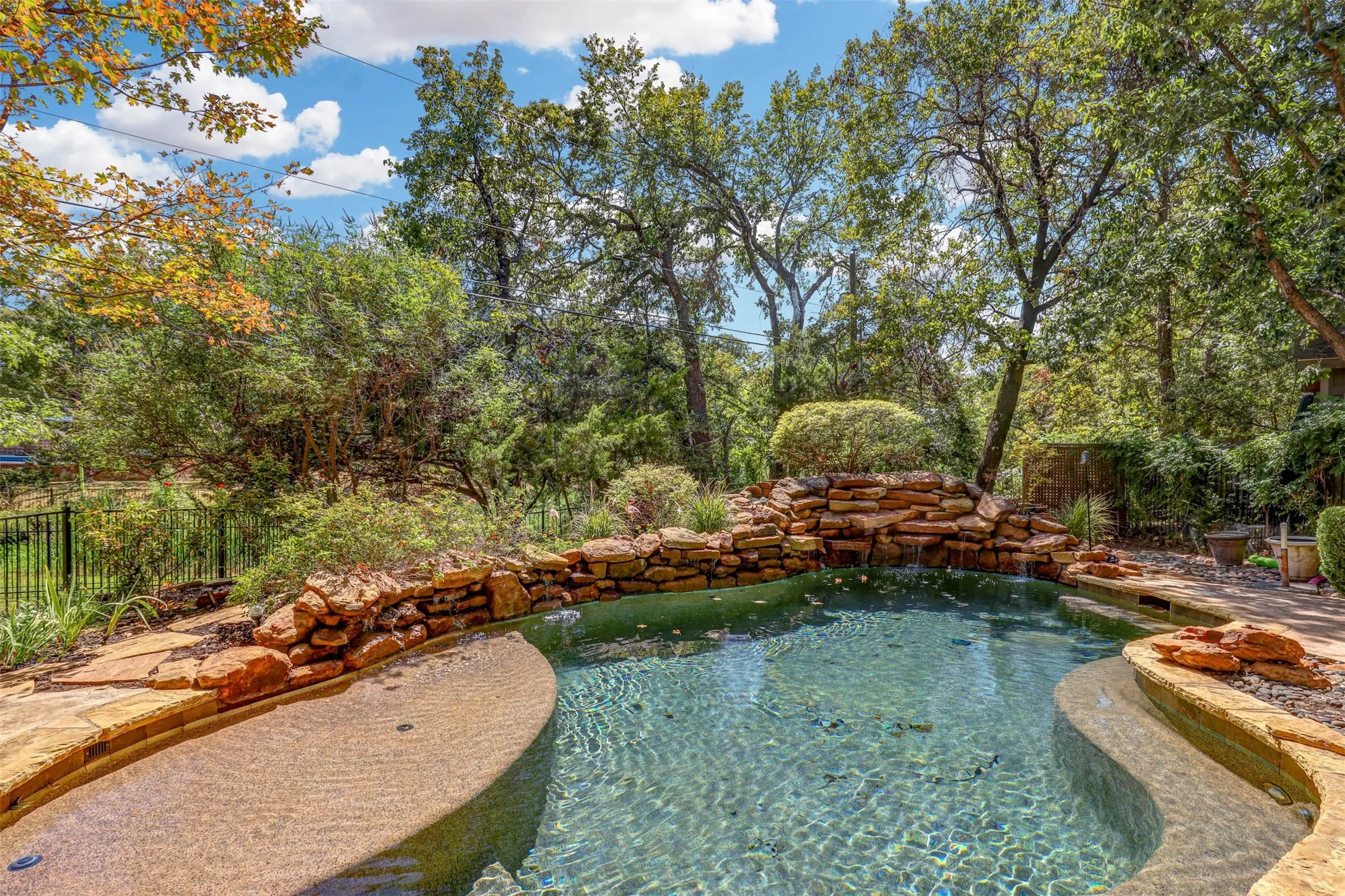 Resort style pool with rock waterfall surrounded by mature trees and natural landscaping.
