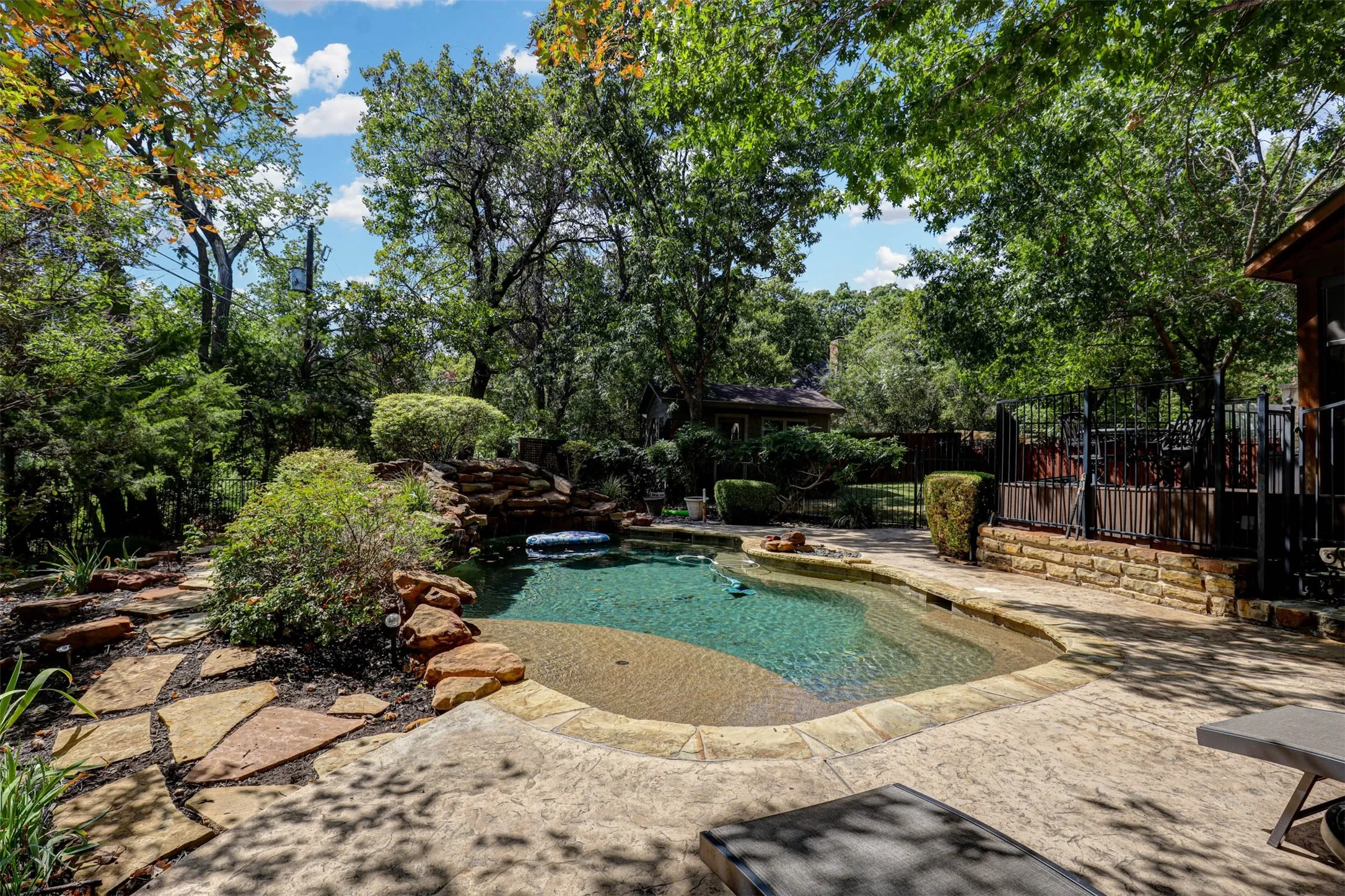 Expansive freeform pool framed by stonework and mature trees.