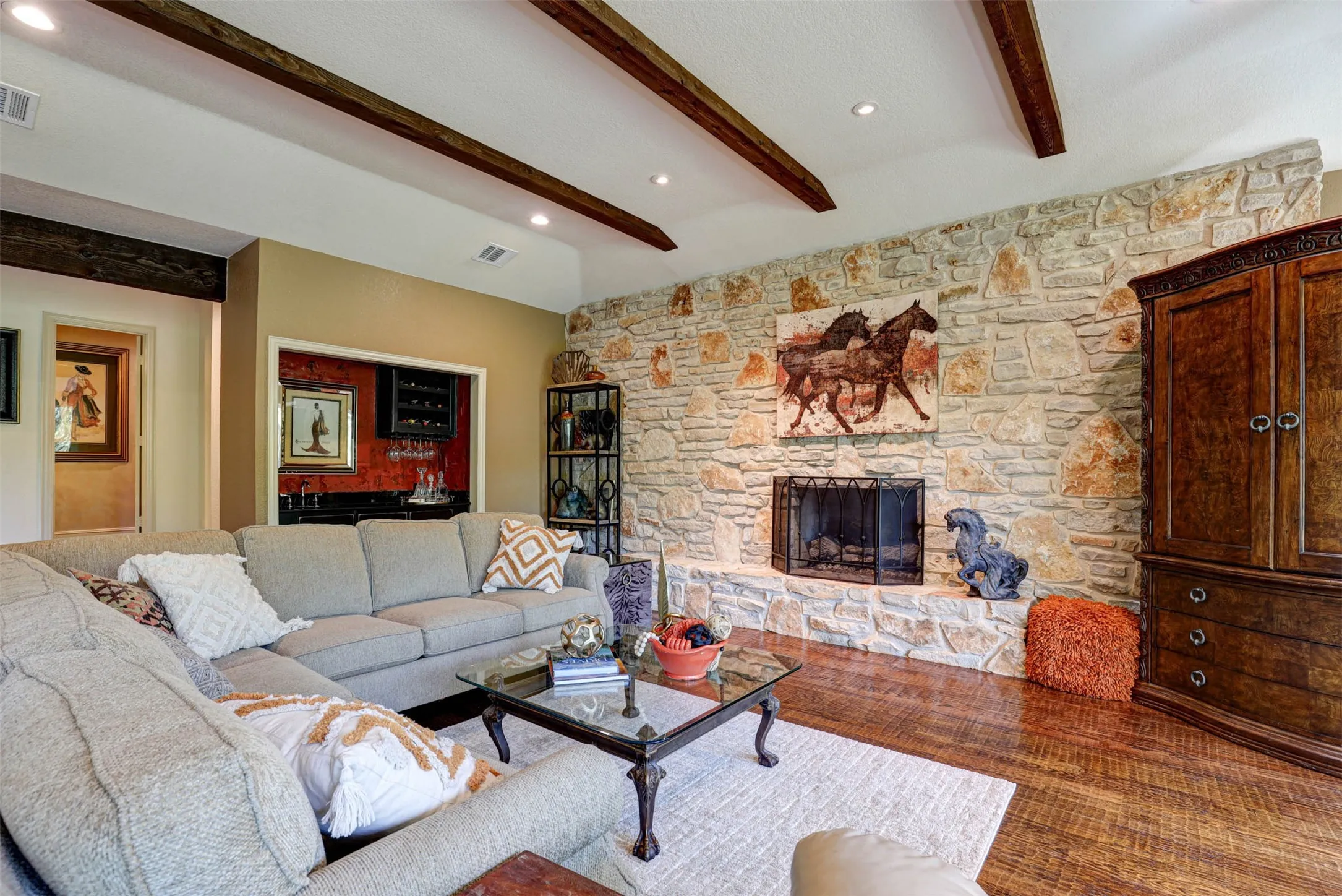Spacious living room with rich wood floors, showcasing stone fireplace, and beam accents.