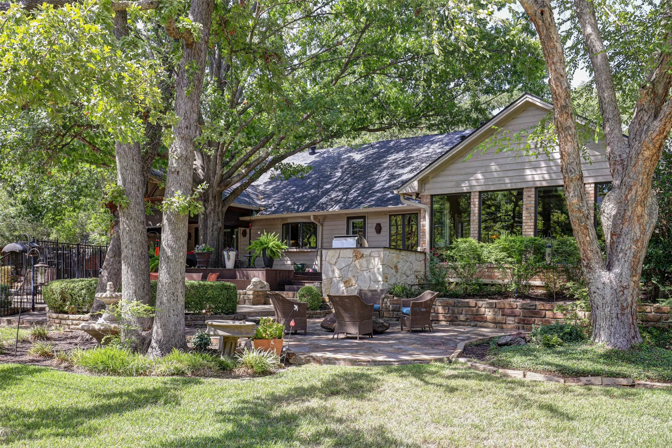 Back of the home with large windows and stone patio, surround by lush landscaping.