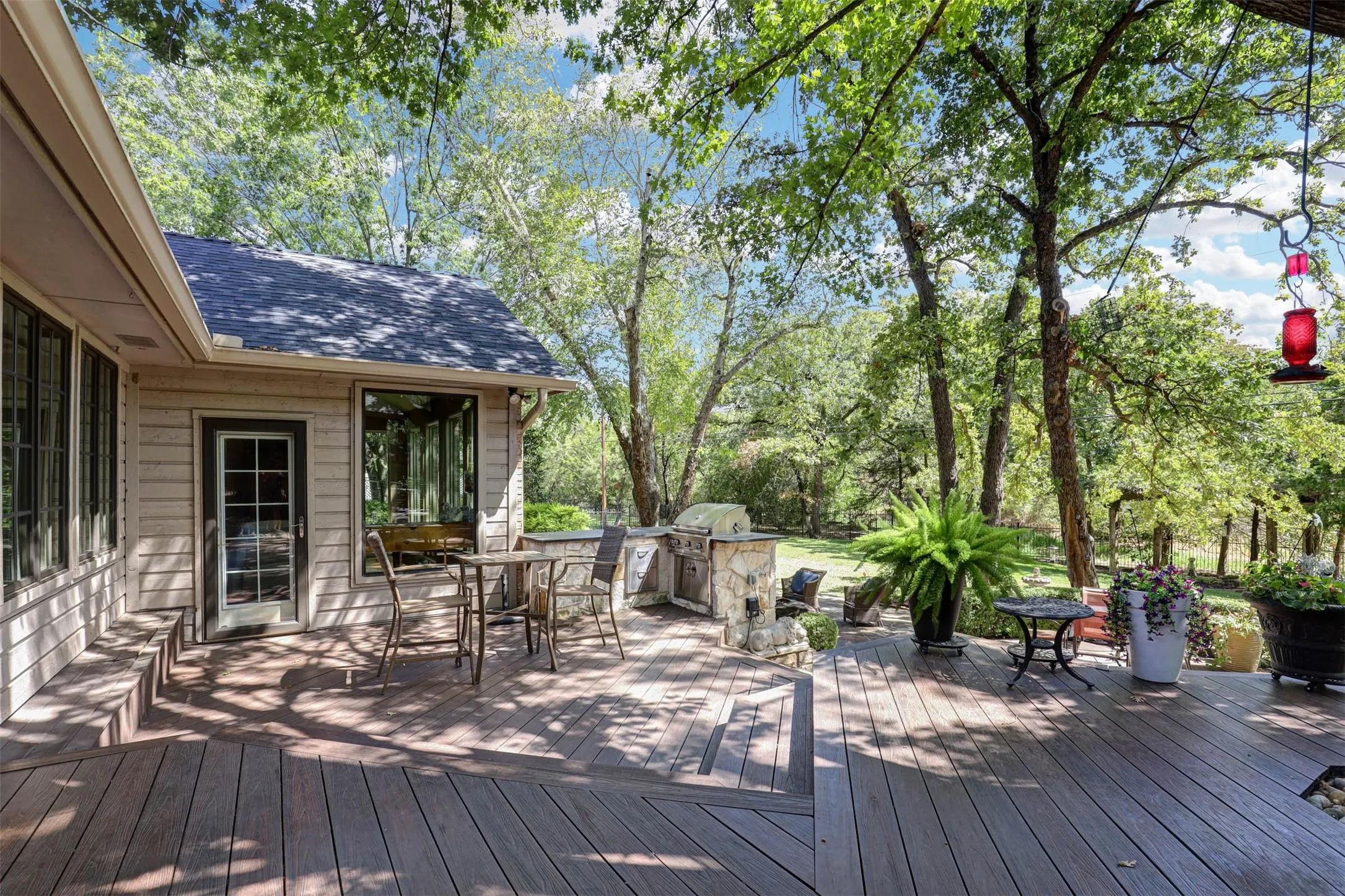Shaded backyard deck surrounded by mature trees, offering multiple seating areas for outdoor living.