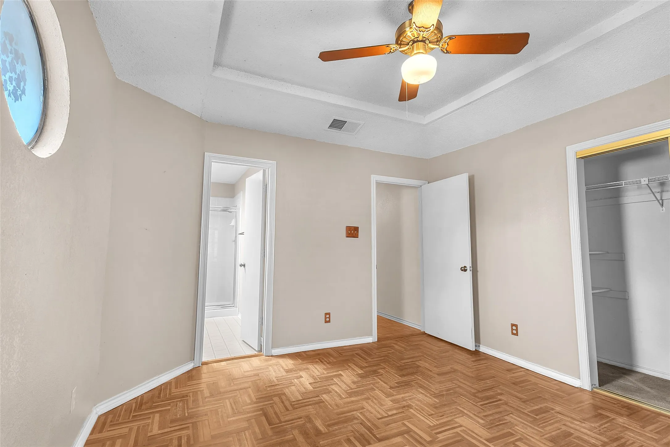 Bedroom with hardwood flooring, a ceiling fan, circular window, and adjoining bathroom; includes closet space and neutral wall colors