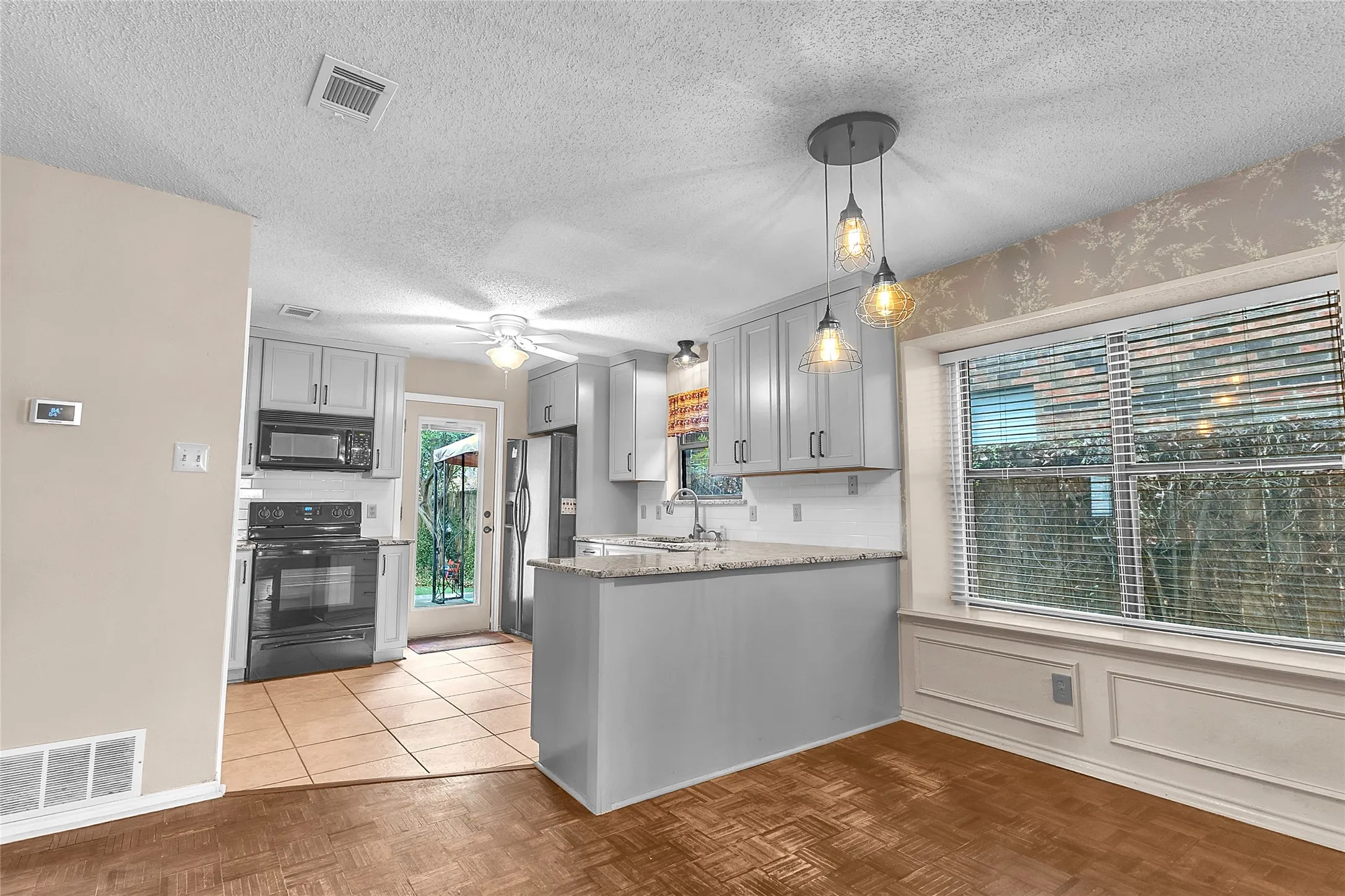 Open-plan kitchen with stainless steel appliances, quartz countertops, recessed lighting, and a view of the backyard through a sliding glass door.