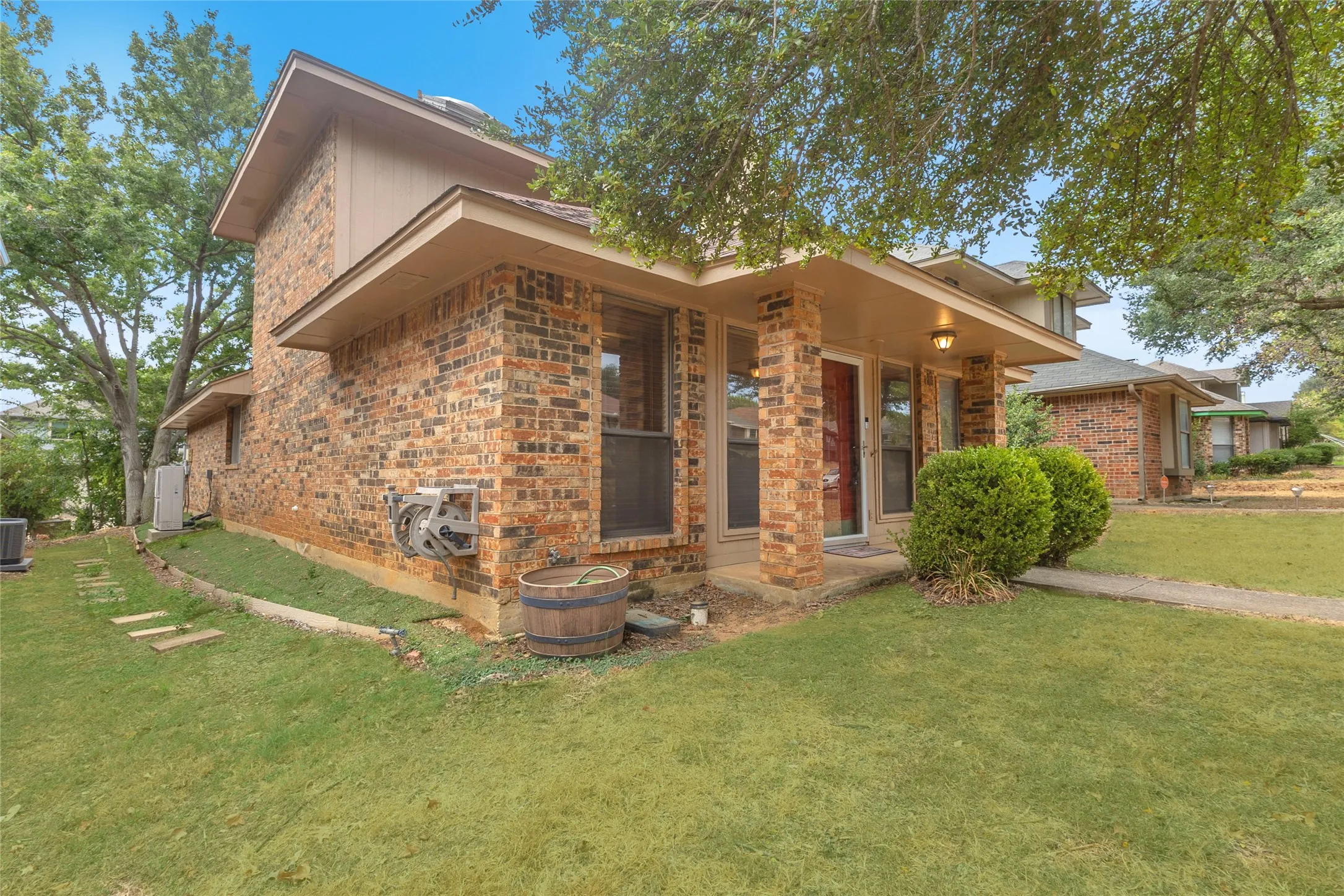 Exterior view of a two-story brick home with a landscaped lawn, shaded entryway, and central air conditioning unit, showcasing a well-maintained exterior.