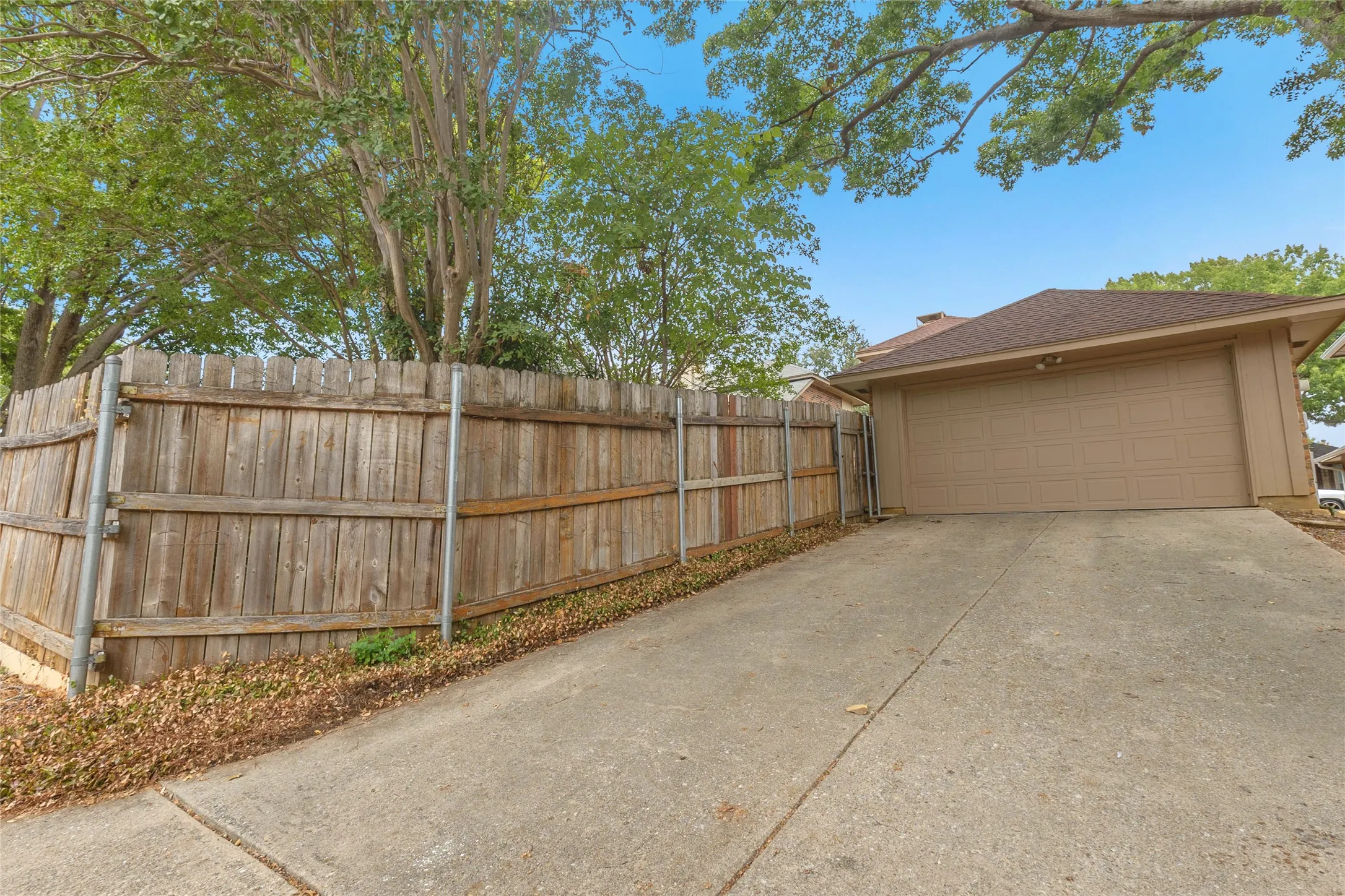 Two-car garage with concrete driveway and wooden fence, surrounded by trees providing a natural setting and increased privacy