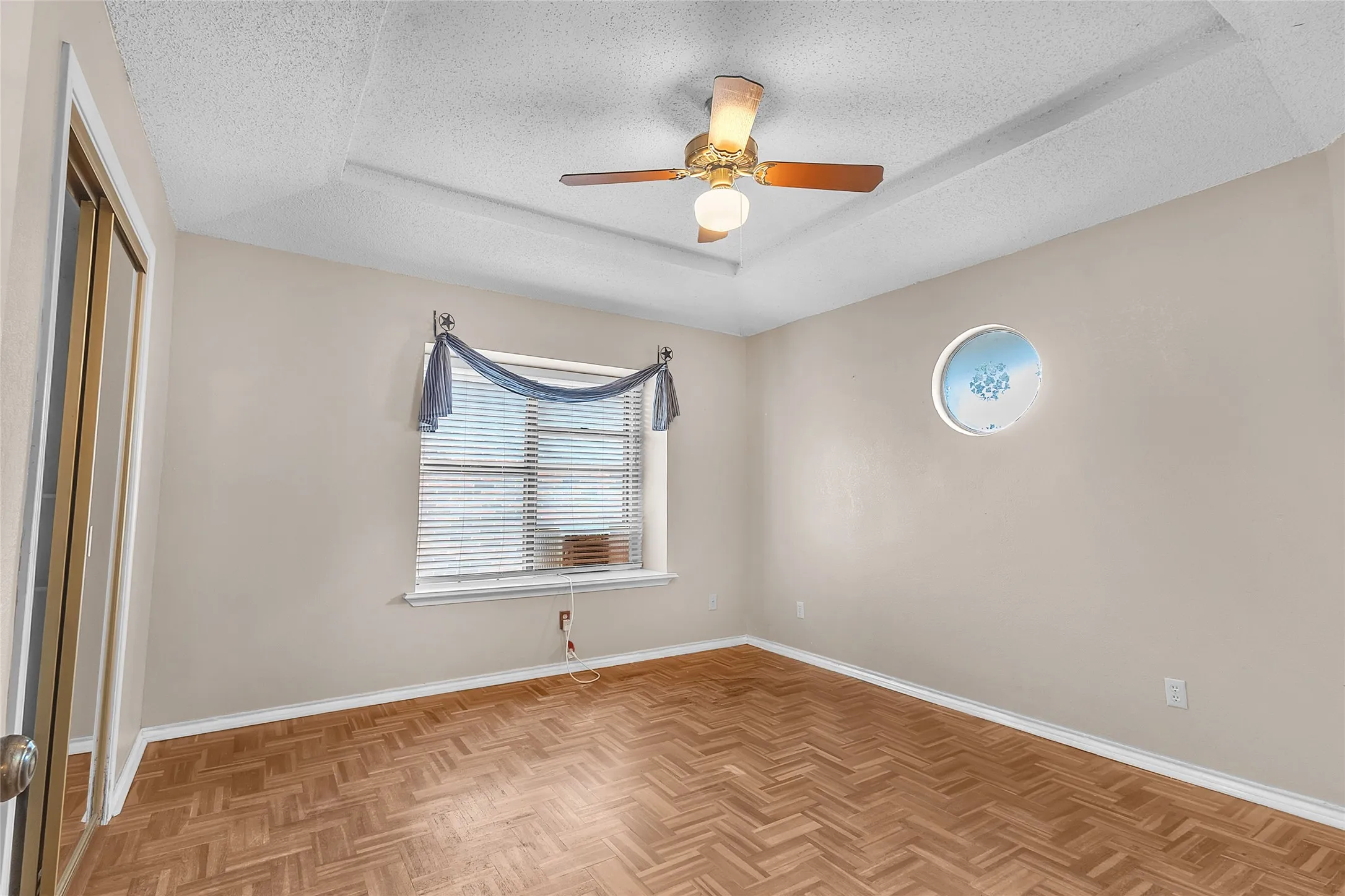 Bedroom with hardwood flooring, ceiling fan, and a decorative circular window providing natural light and a unique architectural detail