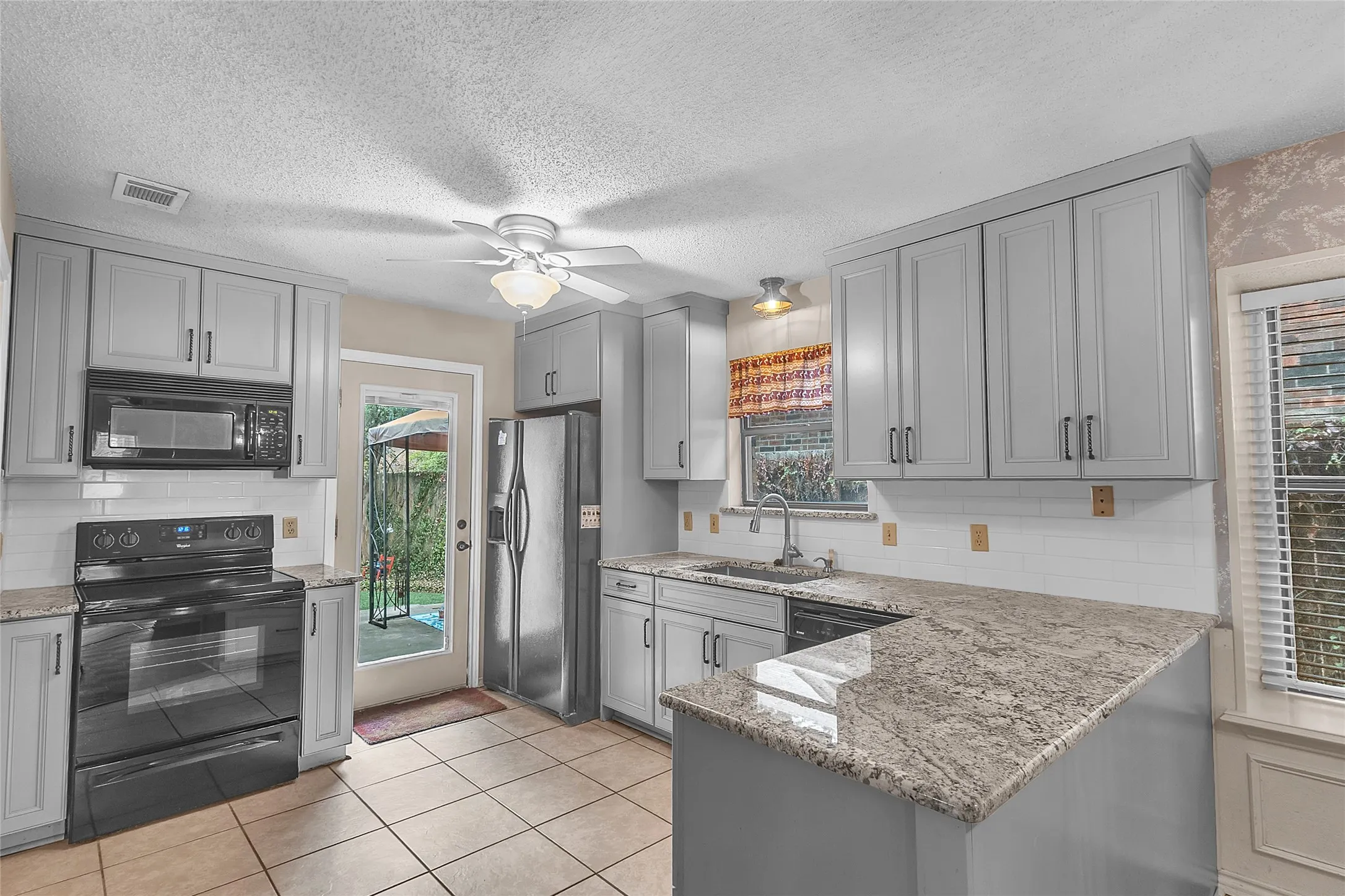 Open-plan kitchen with gray cabinetry, granite countertops, stainless steel appliances, and a sliding glass door for natural light and access to the patio