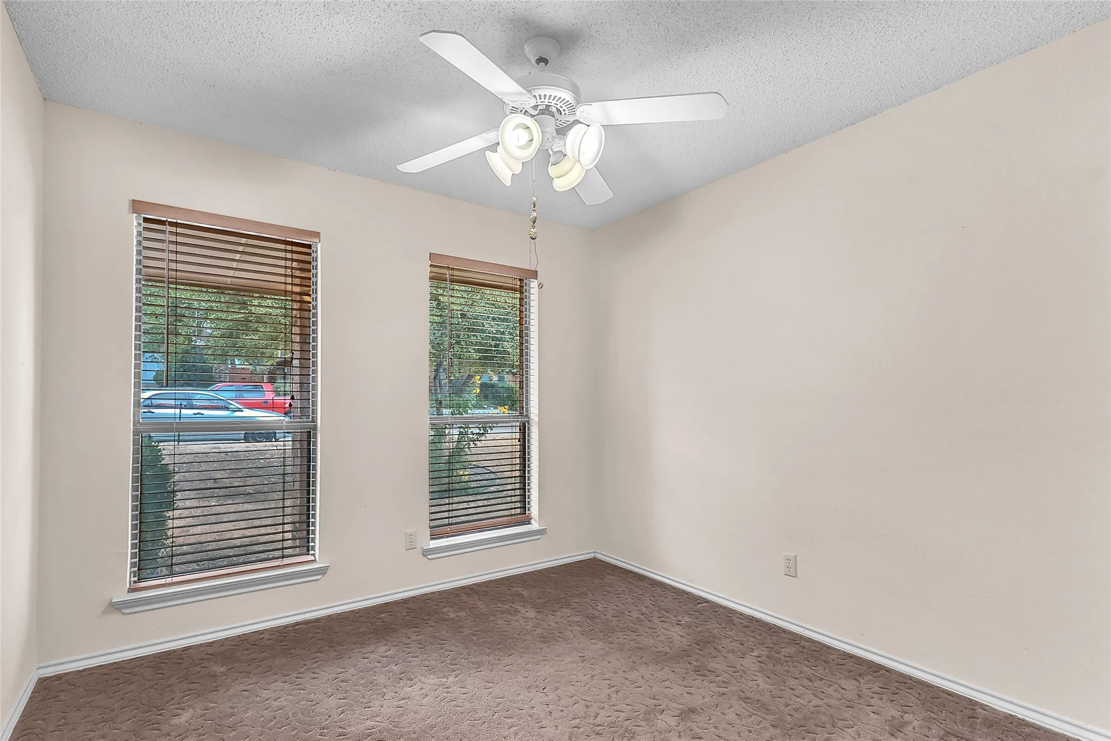 Empty room with two windows, ceiling fan, and beige carpet. Natural light fills the space, creating a bright and airy atmosphere.