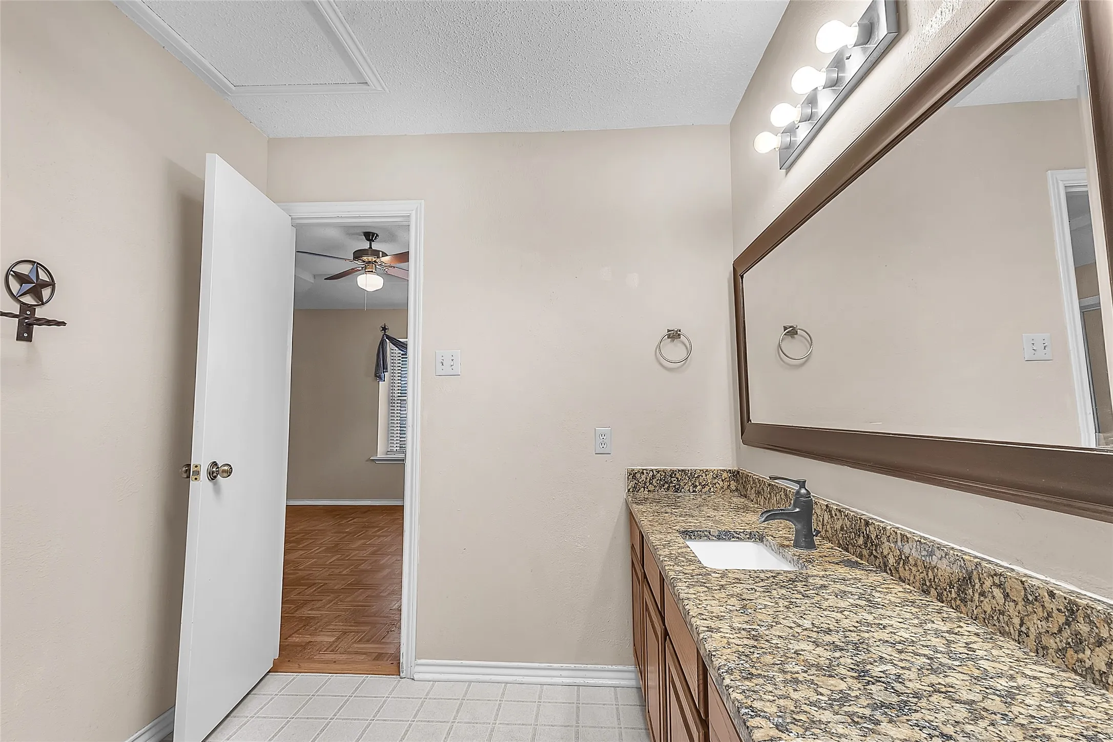 Bedroom with hardwood flooring, a ceiling fan, circular window, and adjoining bathroom; includes closet space and neutral wall colors