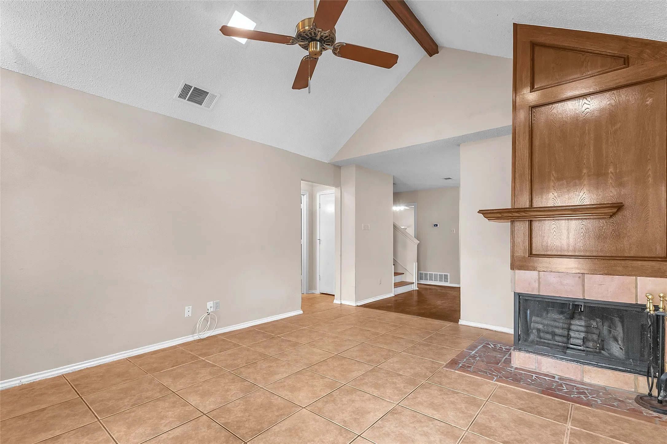 Living room with vaulted ceiling, tiled floor, wood mantel fireplace, and ceiling fan, creating an open and airy layout.