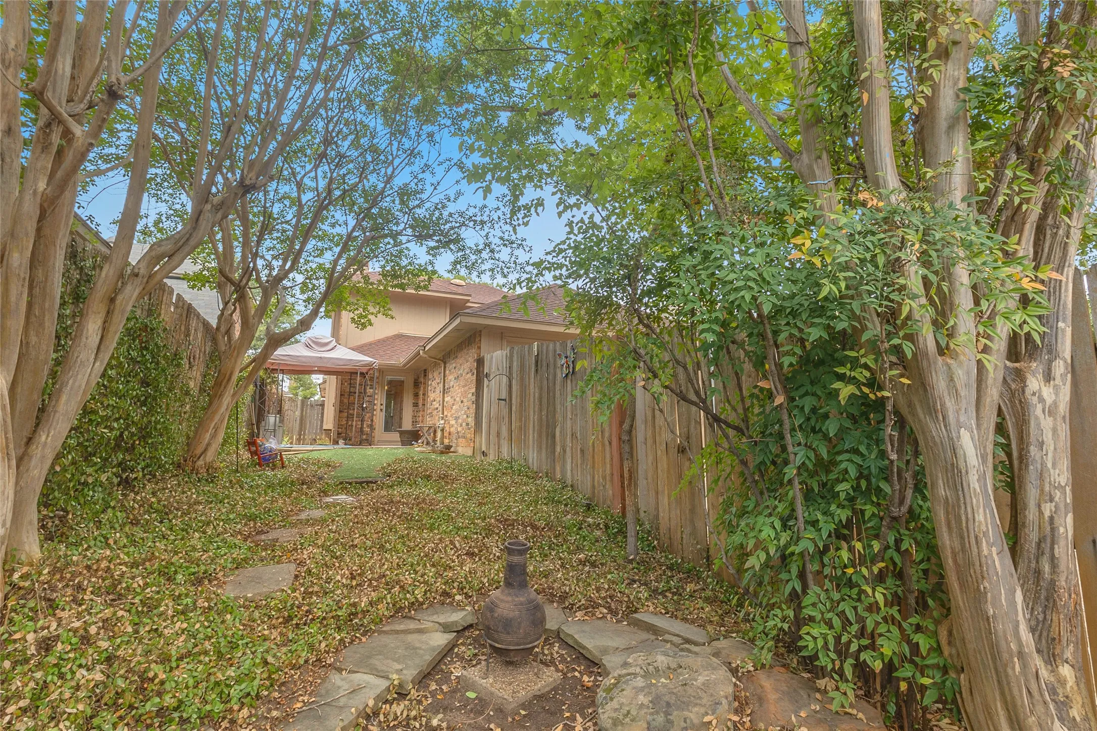 Backyard pathway with stone stepping stones, surrounded by mature trees and vegetation, leading to a covered patio area.