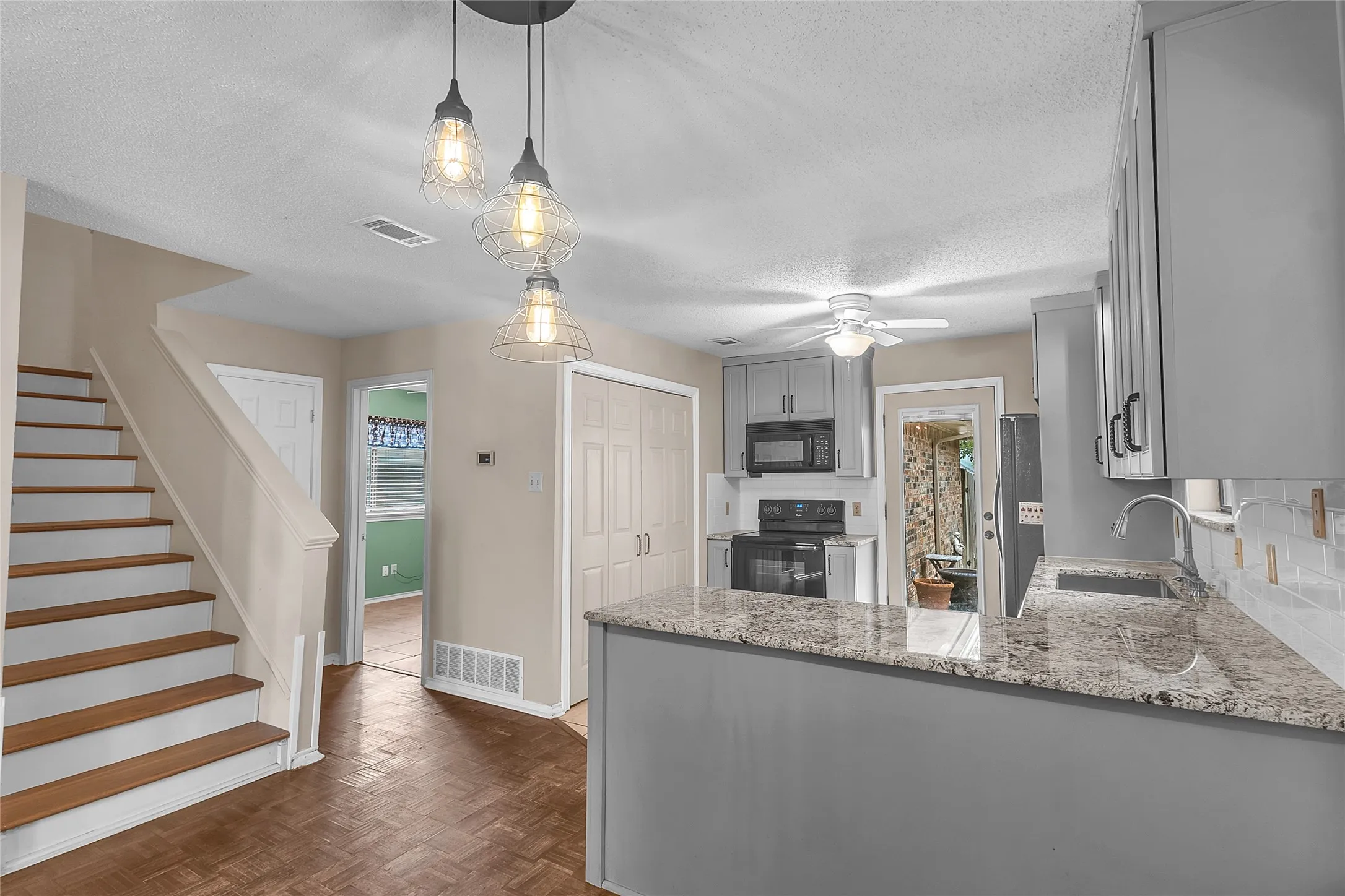 Open-plan kitchen with granite countertops, stainless steel appliances, and recessed lighting adjacent to the stairs and pantry access.