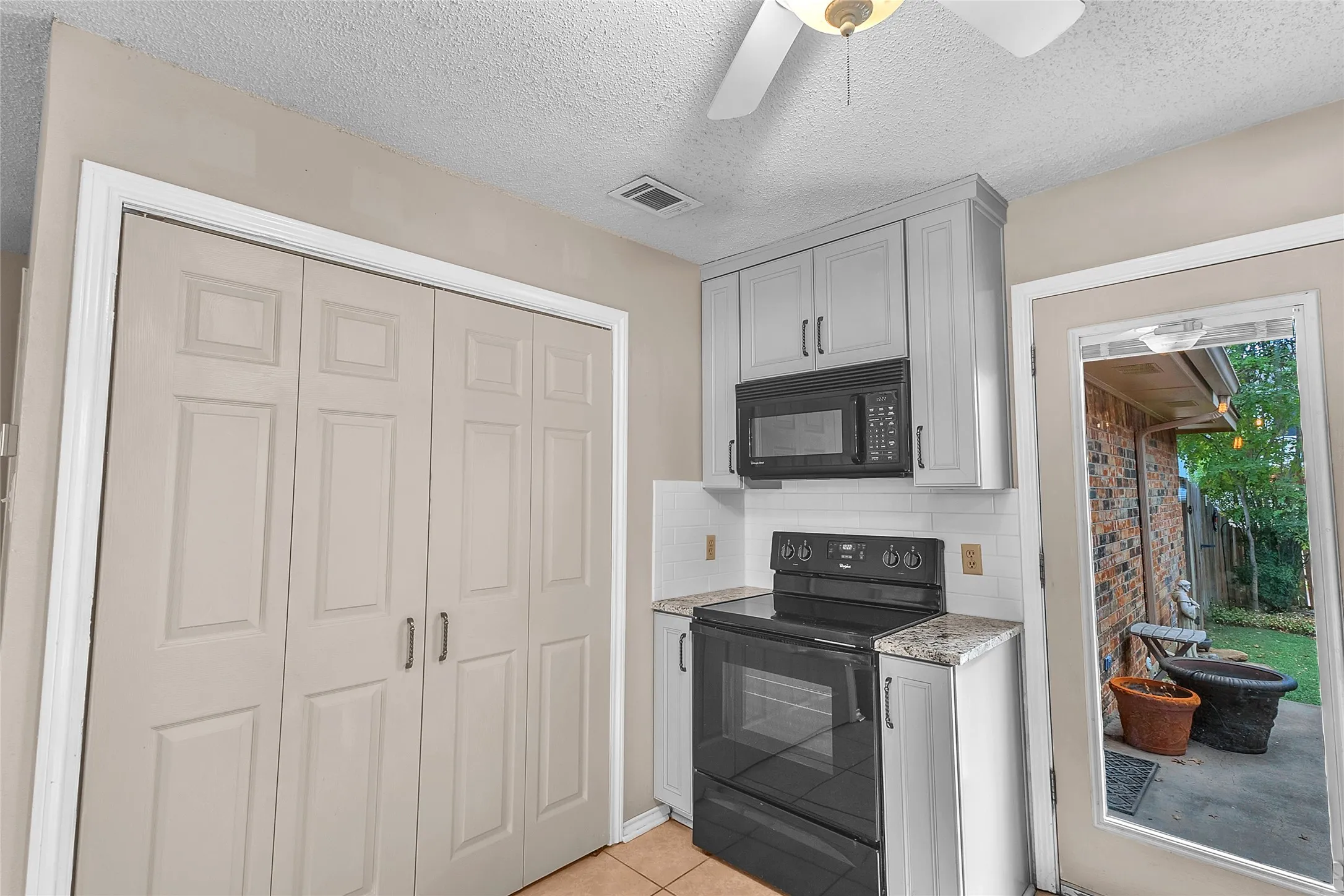 Open-plan kitchen with granite countertops, microwave, stainless steel appliances, and dual closets adjacent to a door leading to the outdoor area