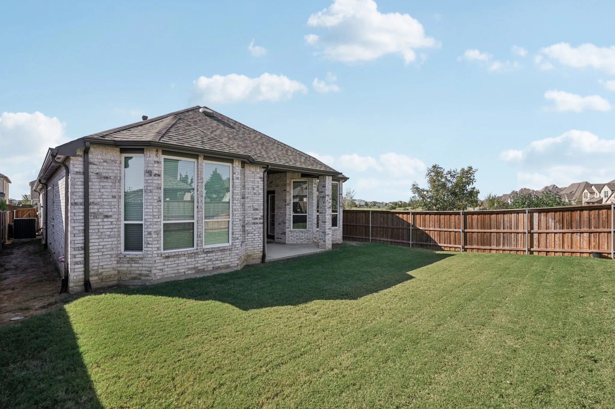 Expansive backyard featuring a manicured lawn, full privacy fencing, and a covered patio area