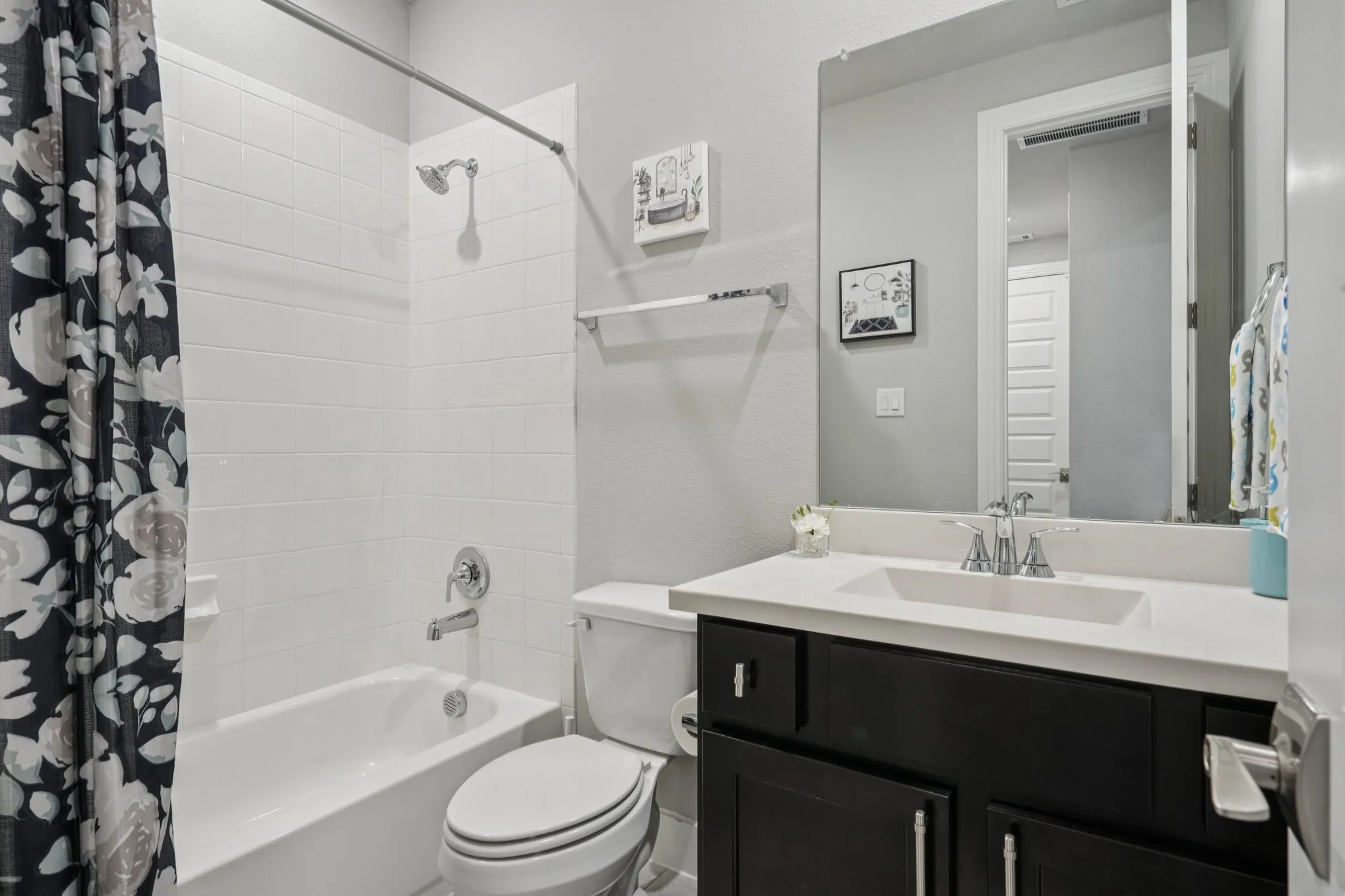 Built-in bathtub with subway tile surround, chrome fixtures, and a dark wood-finish vanity with an integrated sink and light-toned countertop