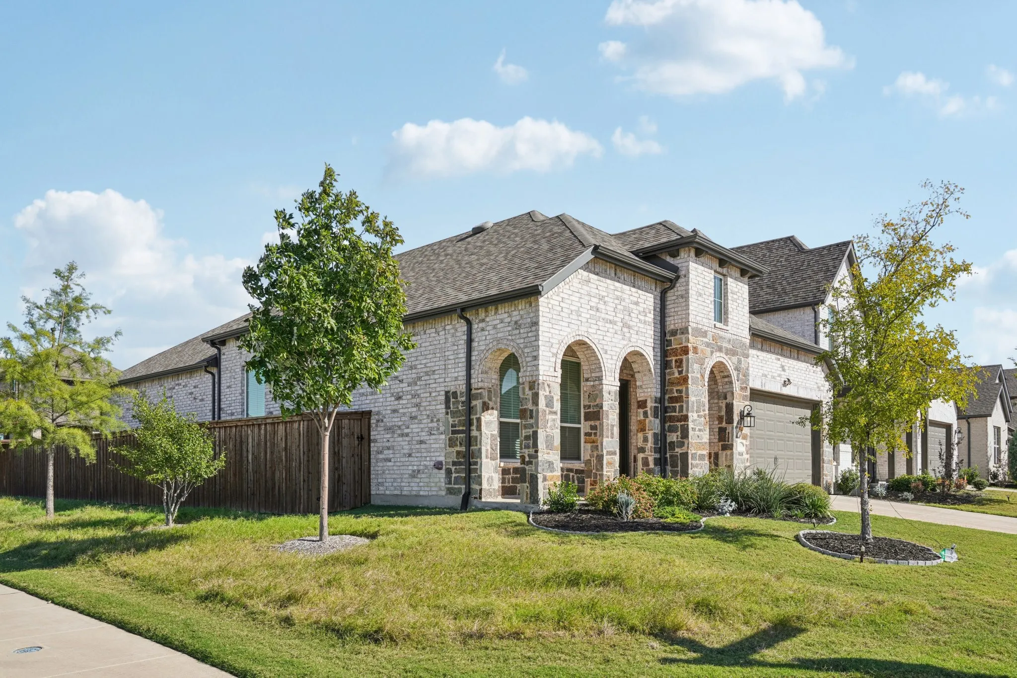 Stone and brick exterior with arched window openings, a dark shingle roof, and an attached garage