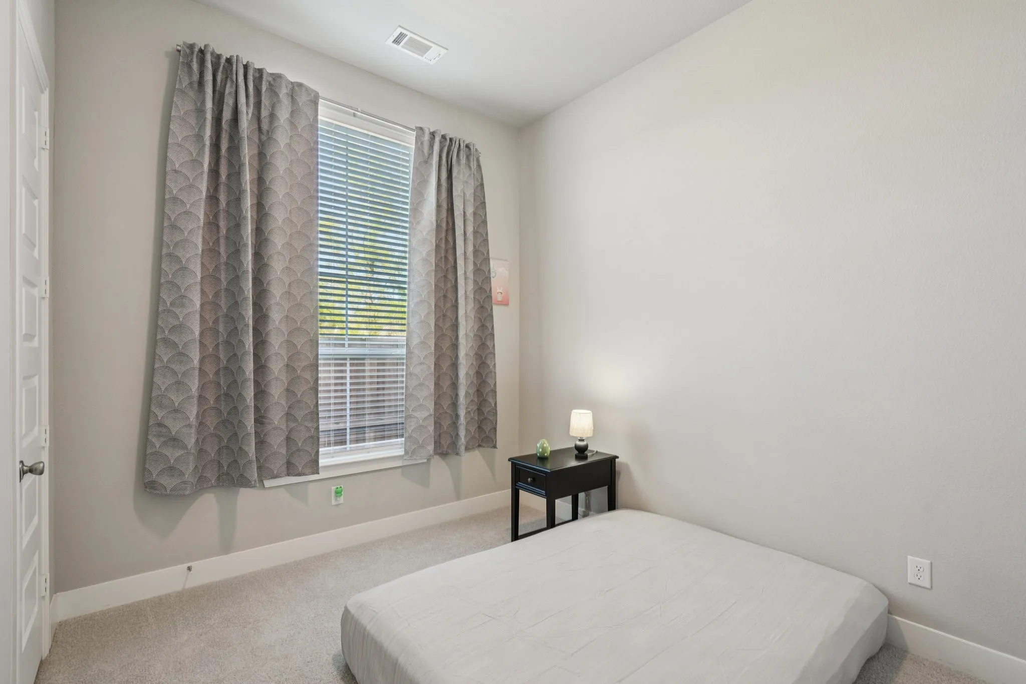 Neutral-toned walls, a single window with blinds, and light-toned carpet