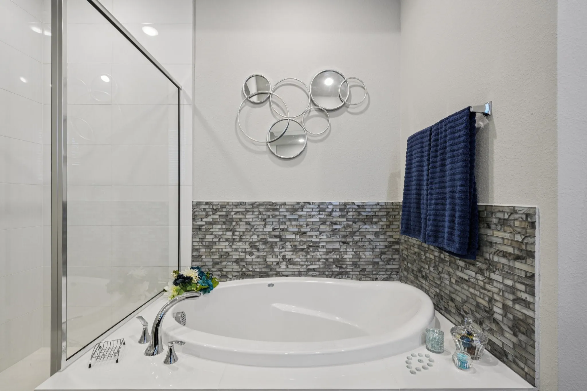 Built-in soaking tub with deck-mounted faucet, mosaic tile surround, and a glass-enclosed shower