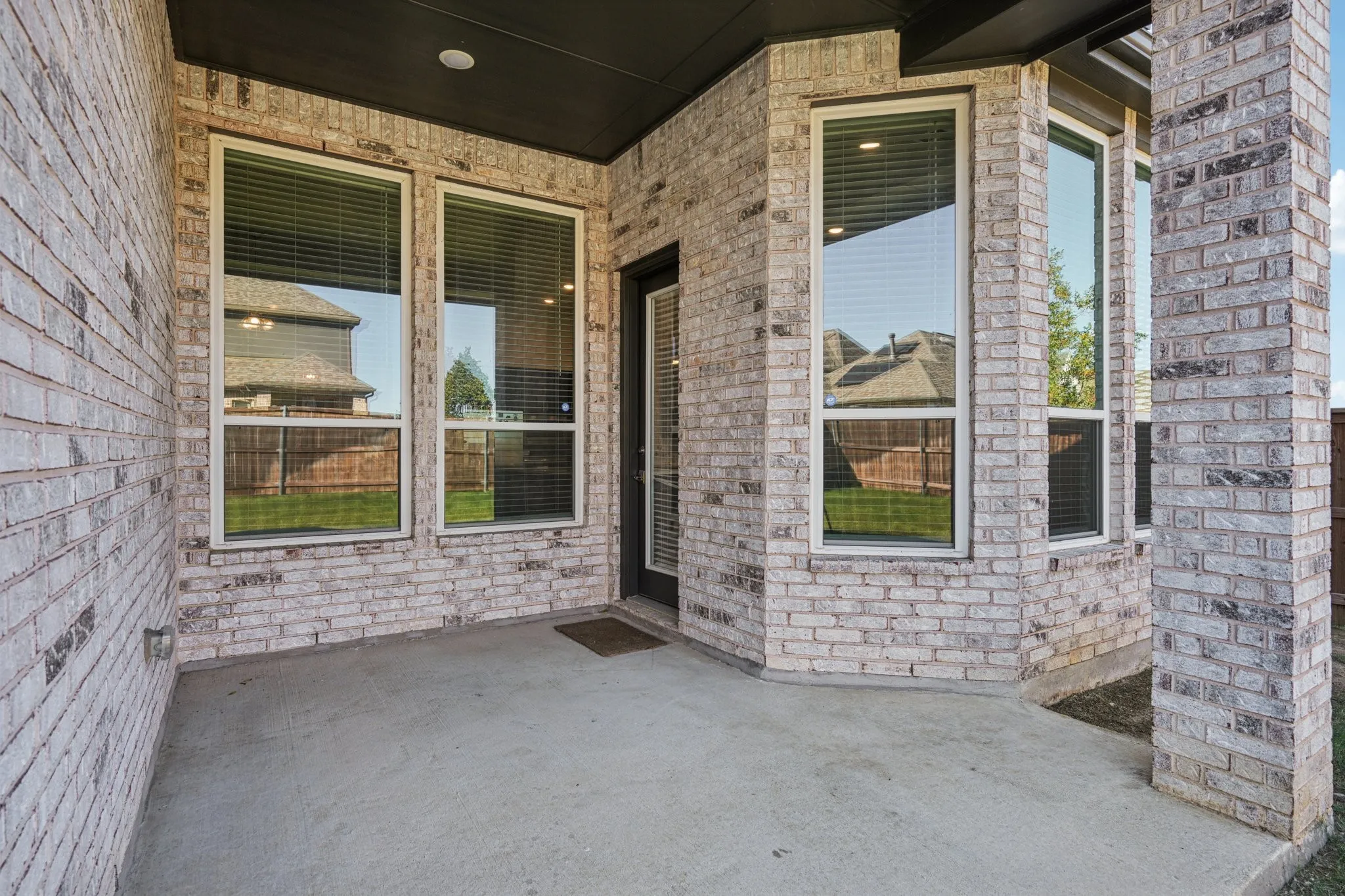 Covered patio featuring a concrete surface, brick exterior, multiple windows, and a glass-paneled door
